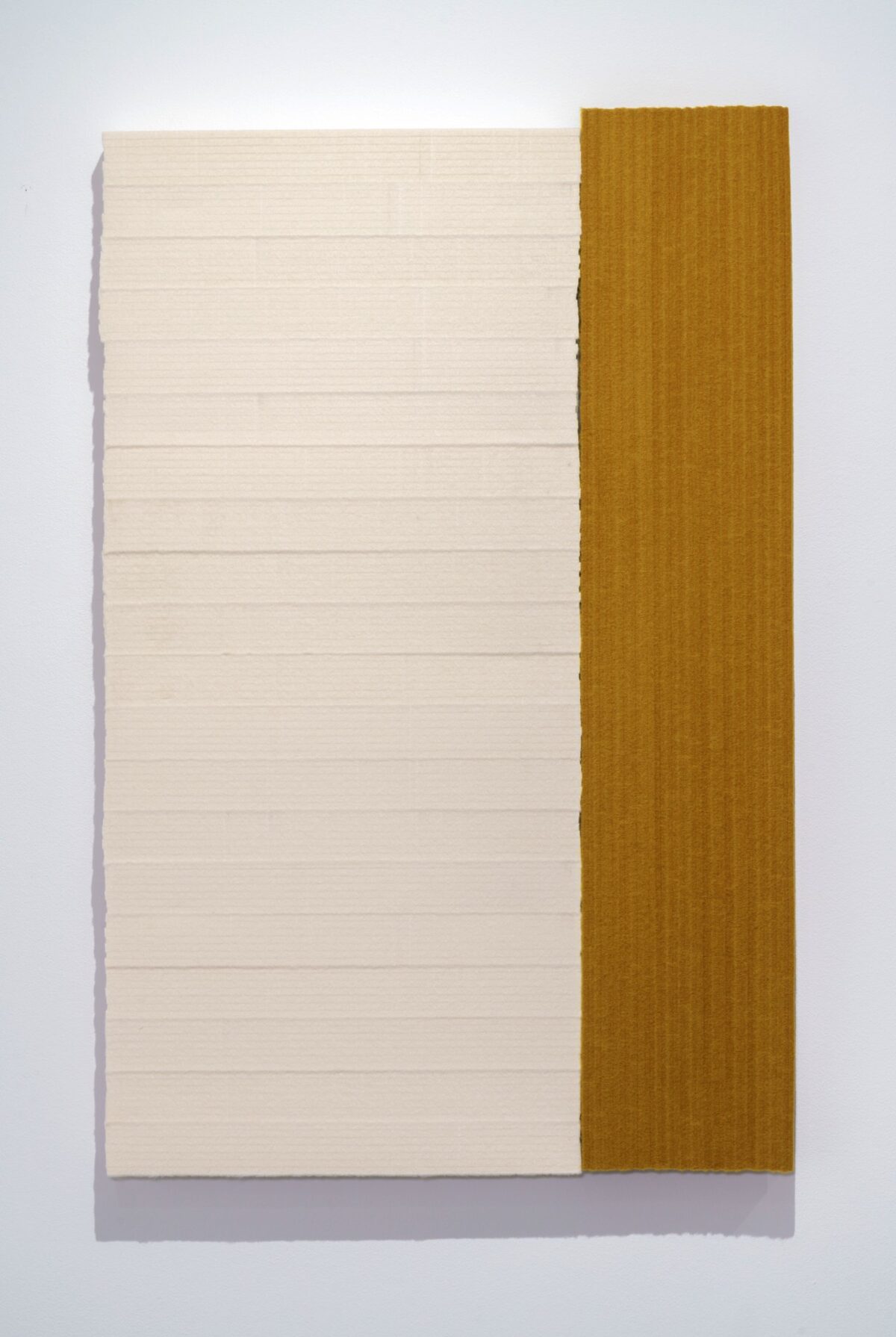 Two panels of industrial felt mounted on plywood: a cream-colored panel with horizontal striations on the left, adjoining a warm ochre panel on the right. The rectangular composition is set against a light background, casting a subtle shadow.