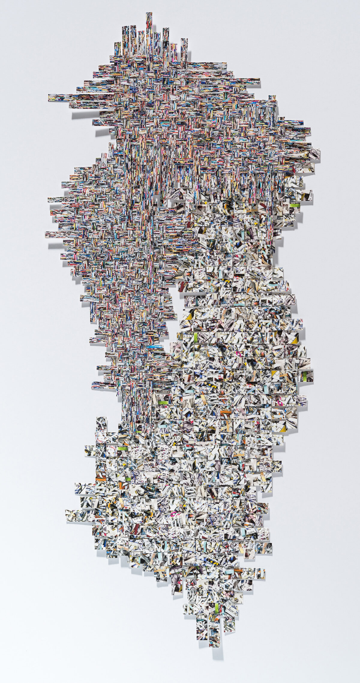A vertical collage composed of hundreds of small photographic fragments arranged in a dense, organic pattern. The upper portion features tightly layered colorful images creating an intricate woven texture, while the lower half transitions to predominantly white and grayscale fragments that taper toward the bottom, creating a cascading effect against a white background.