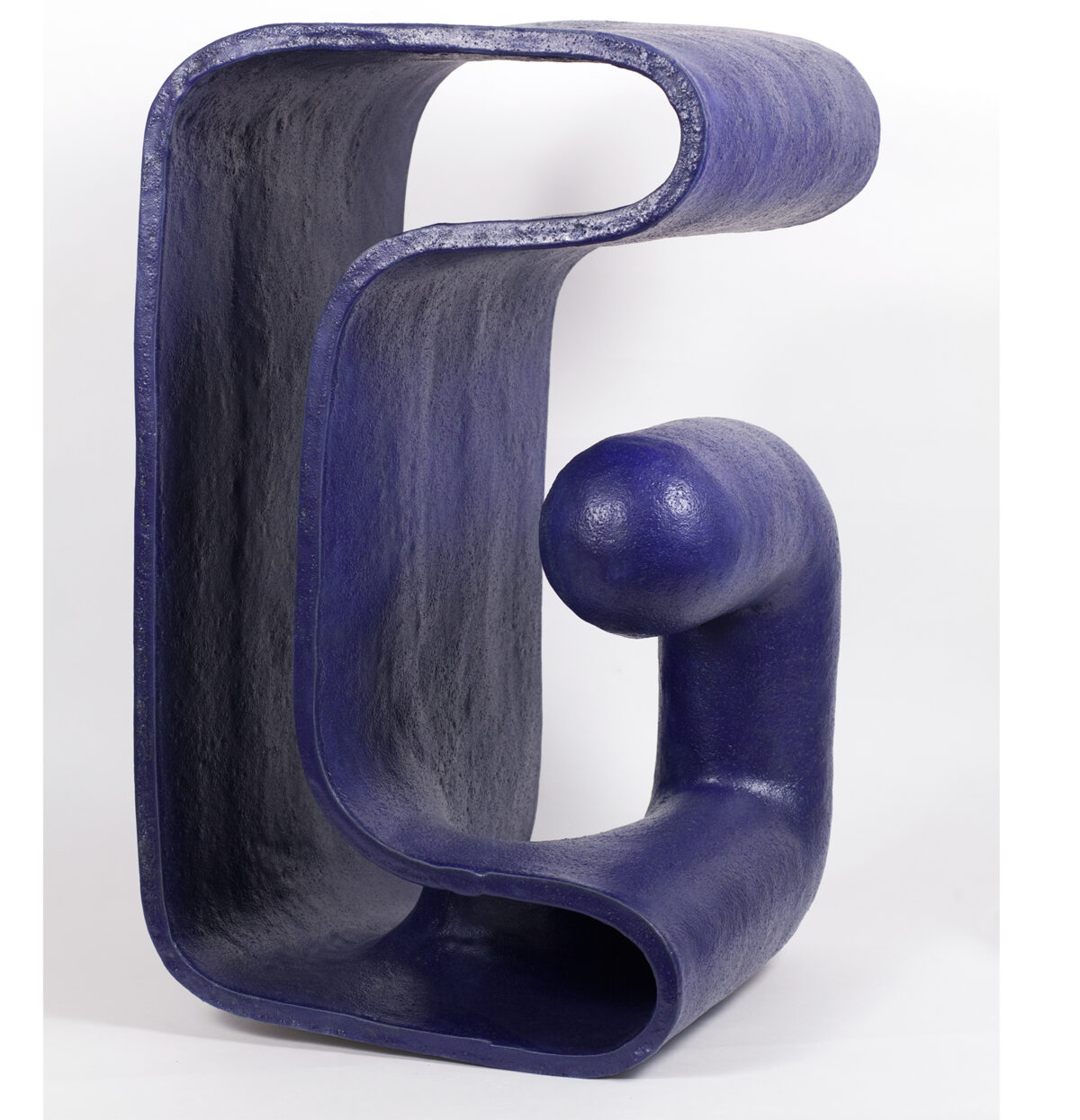 A deep blue ceramic sculpture with a glossy glaze featuring an abstract, organic form that resembles a stylized finger or curved gesture. The piece has smooth, rounded surfaces with hollow sections and a bulbous protrusion, creating a dynamic three-dimensional composition against a white background.