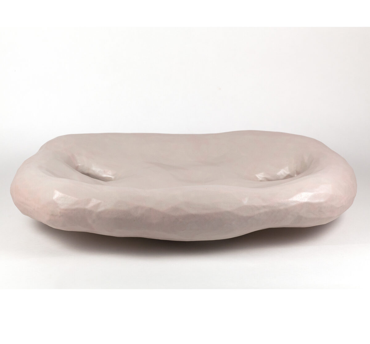 A pale pink ceramic bowl with an organic, elongated form featuring two shallow indentations across its curved surface, finished with a subtle gloss glaze.