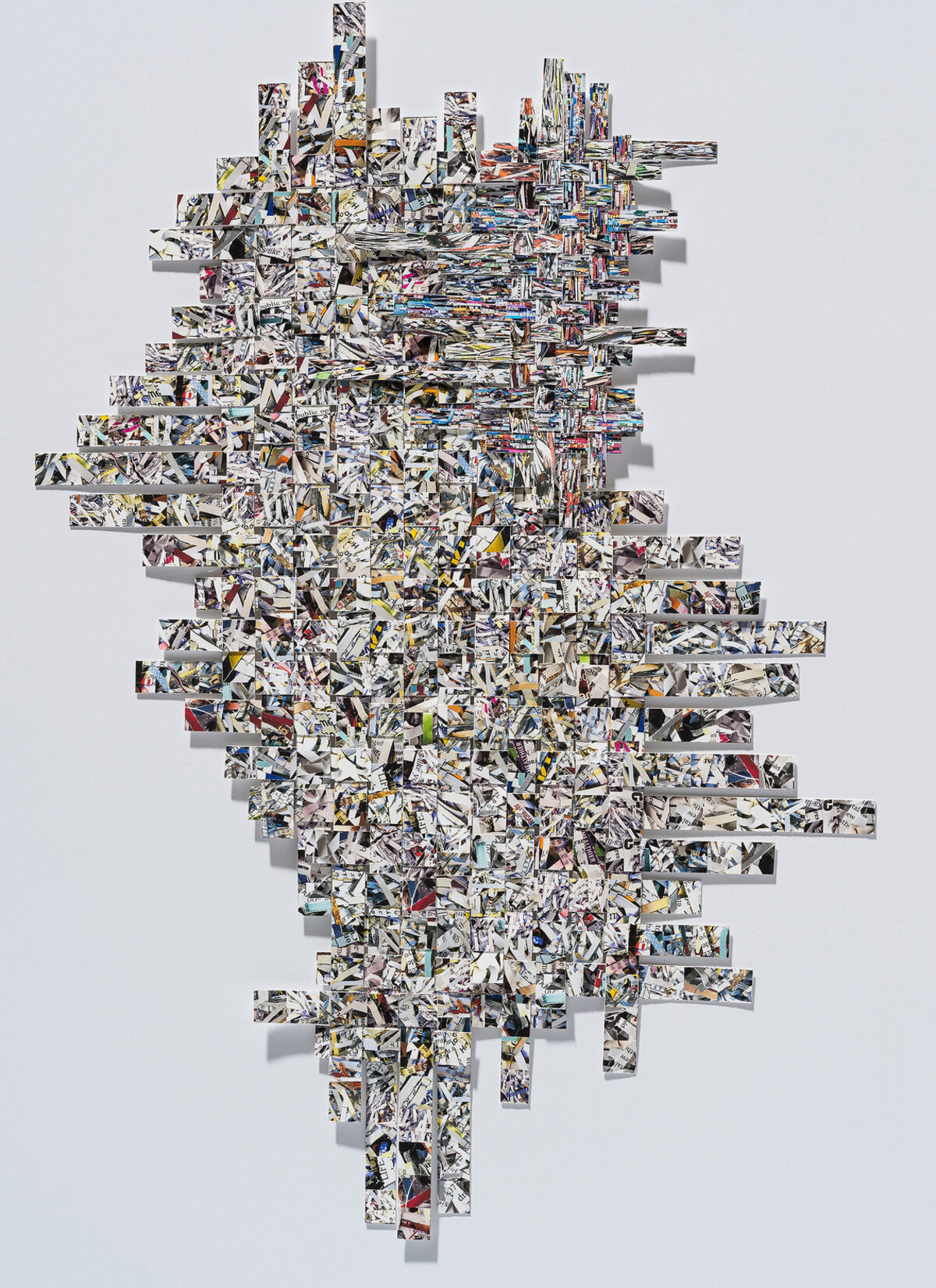 A large-scale collage composed of hundreds of rectangular strips of printed images arranged in a staggered, woven pattern against a white wall. The strips, predominantly black and white with occasional color accents, create a dense, interlocking composition that shifts between structured geometric formations and organic, flowing arrangements. Shadows cast by the protruding elements add depth and dimensionality to the work.