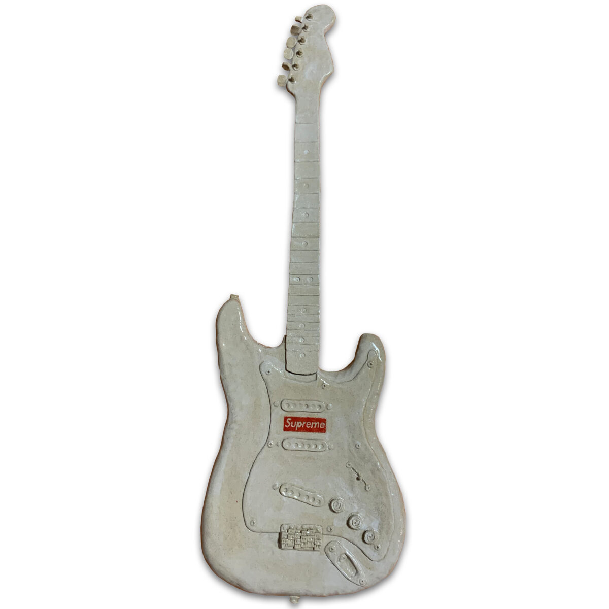 A ceramic electric guitar rendered in pale gray and white glazed clay, featuring a sculpted body with three pickup coils, control knobs, and a bridge, topped with a detailed neck and headstock. The guitar bears a small red rectangular label on its body and displays subtle surface variations suggesting hand-finishing and firing.