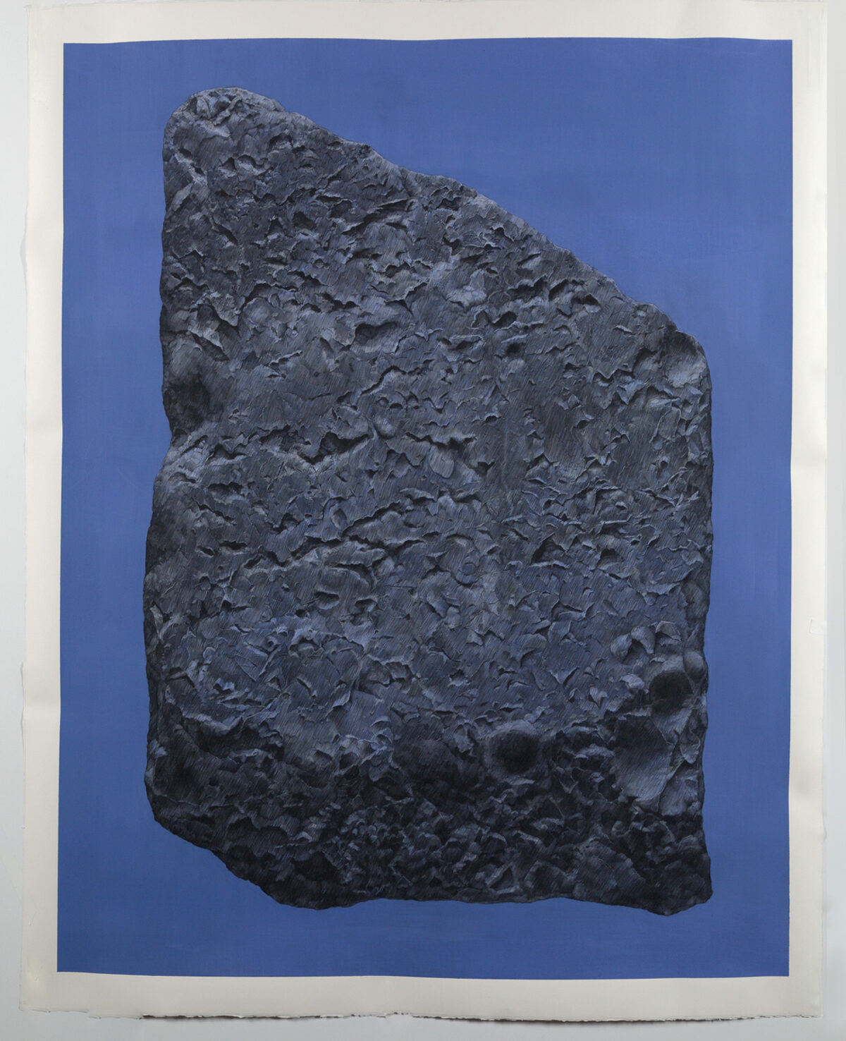 A dark gray textured stone fragment positioned vertically against a deep blue background, its rough surface densely carved with linear marks and patterns that create an intricate, weathered appearance.