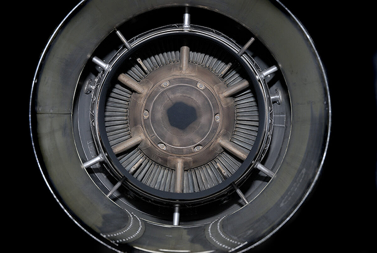 Concentric circular view of a mechanical turbine or engine intake, rendered in grayscale. Radiating fins and metallic components create a hypnotic, symmetrical pattern receding toward a dark central aperture, photographed directly from above against a black background.