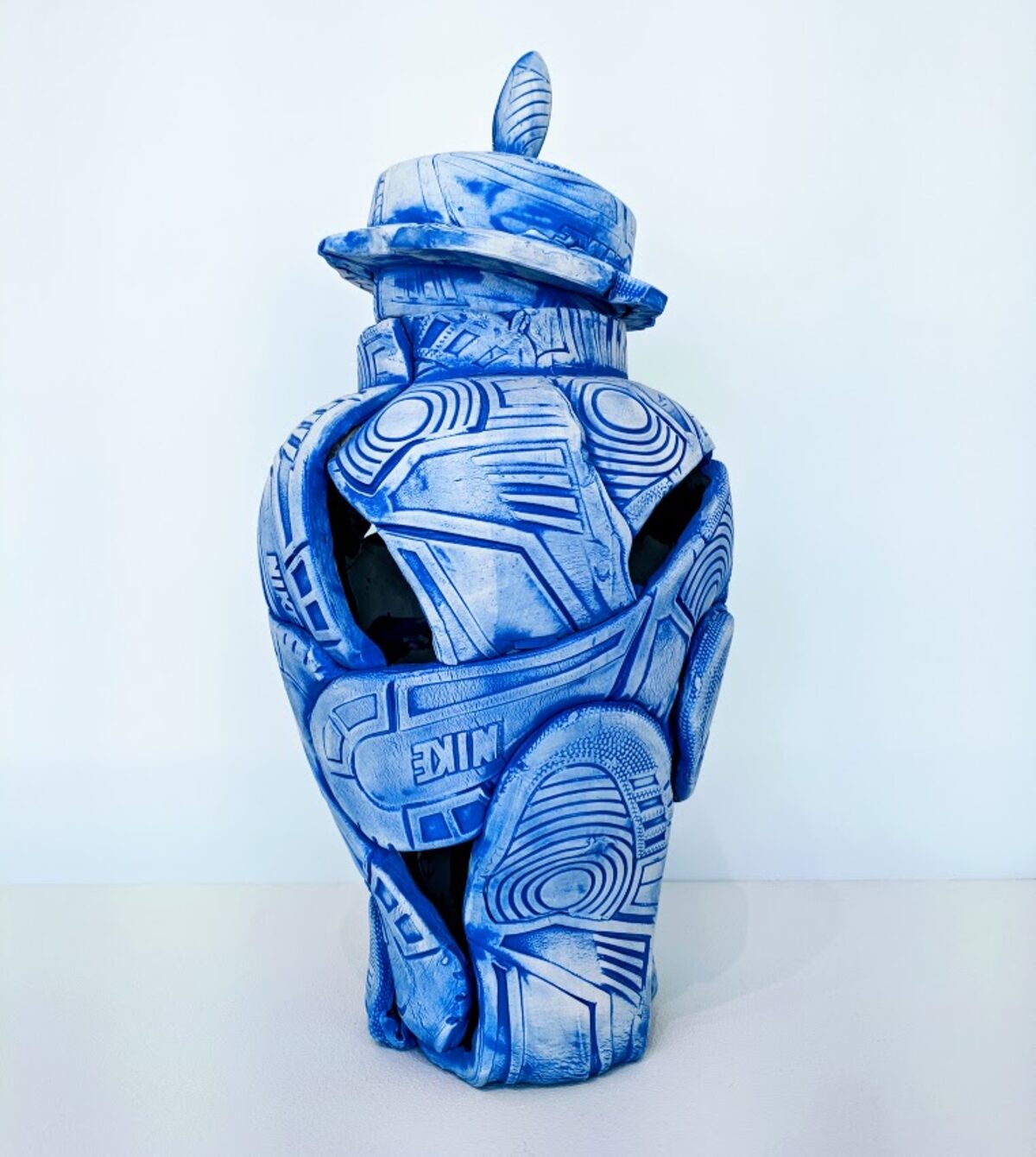 A blue and white porcelain vessel shaped like a deconstructed sneaker, decorated with geometric patterns and concentric circles in the style of Delft pottery. The form features an opening at the center with a lidded top piece, creating a sculptural object that merges functional vessel design with contemporary street culture imagery.