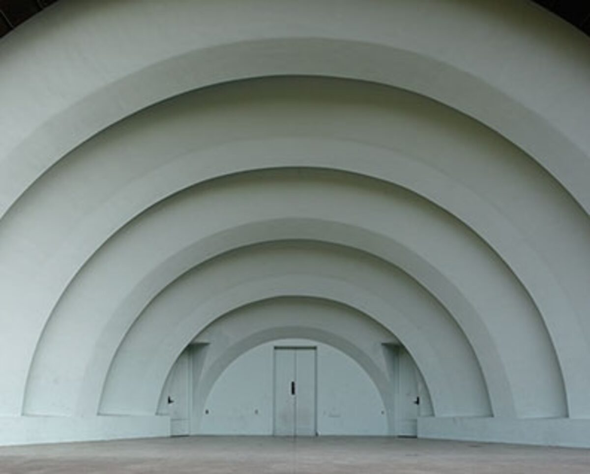 A series of concentric white arched structures recede toward a distant doorway in the center, creating a tunnel-like perspective. The geometric composition emphasizes depth and symmetry through repeated curved architectural forms against a minimal, monochromatic interior space.