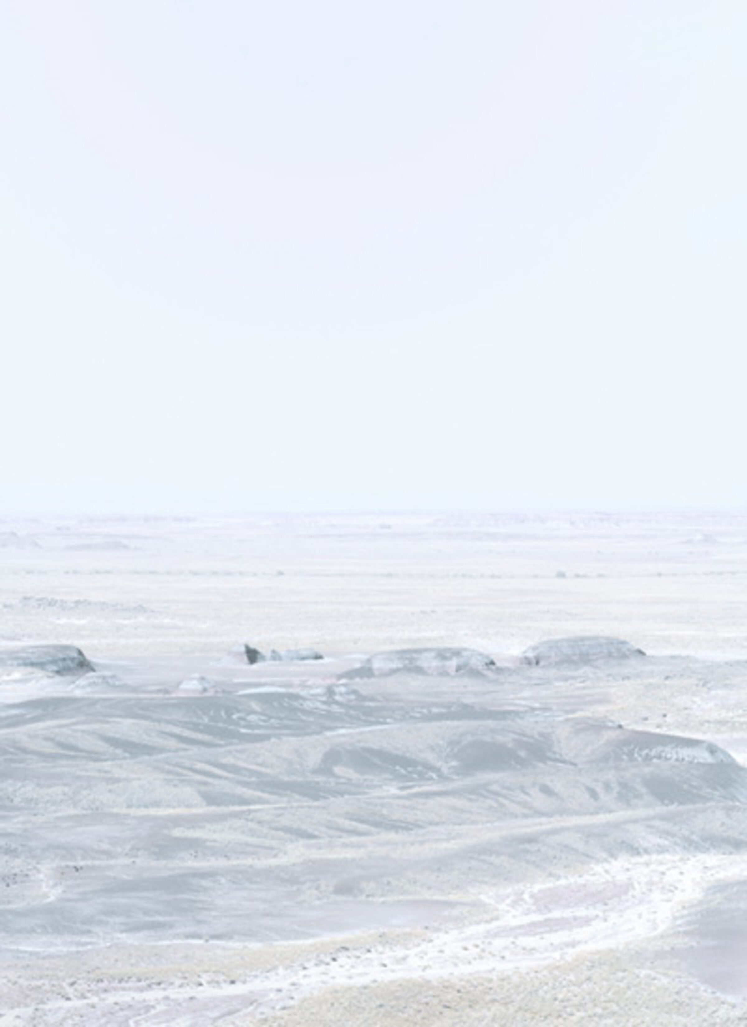 Minimalist coastal landscape with layered horizons of pale gray and white tones. Rocky outcroppings and sandy beach dissolve into misty atmosphere, creating a subtle, almost monochromatic composition that emphasizes atmospheric depth and geometric abstraction.