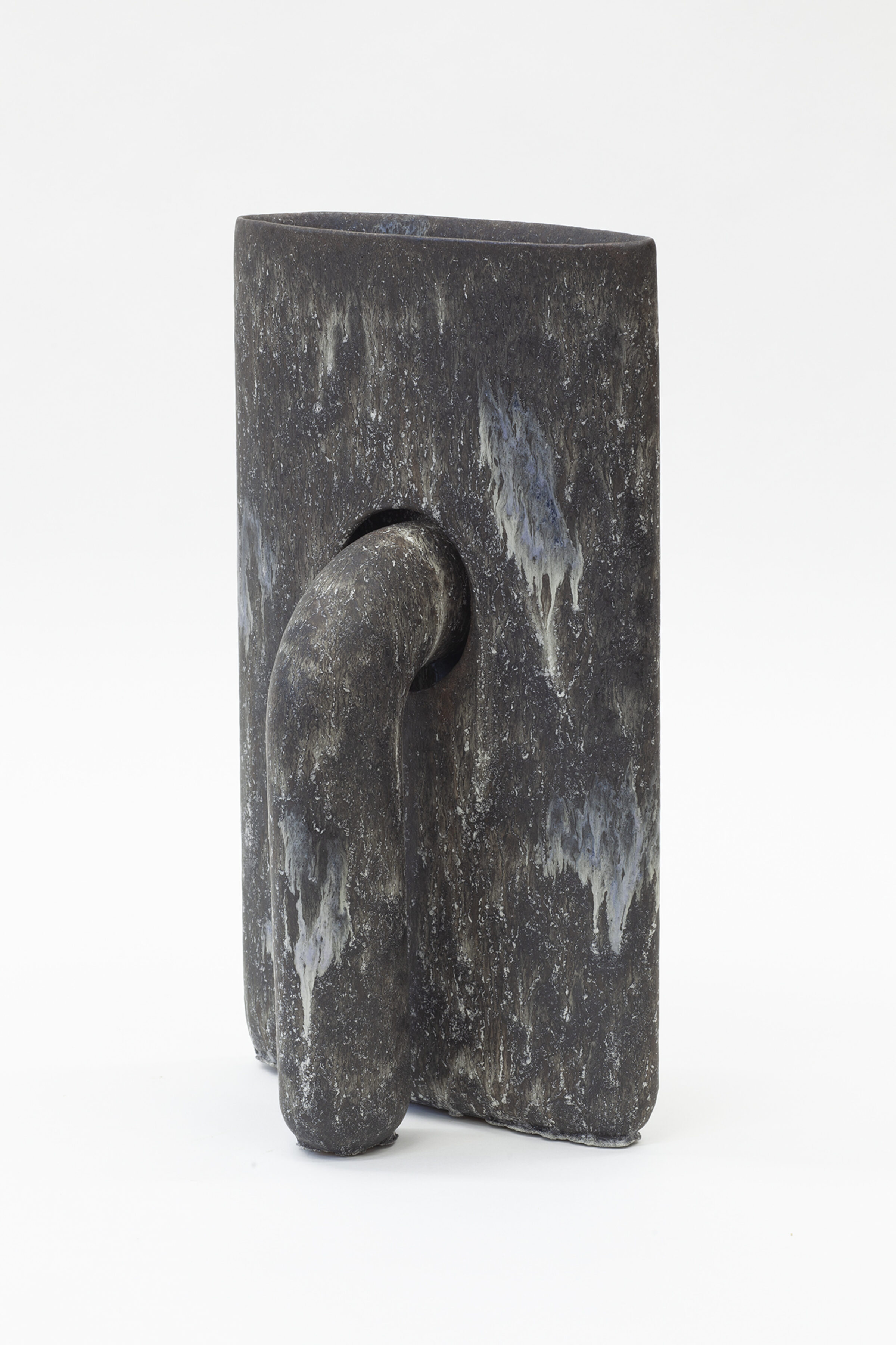 Dark gray stoneware vessel with a rectangular body featuring weathered white streaking across its surface. A curved, organic form protrudes from the front, creating an abstract sculptural composition that suggests both natural and figural elements.