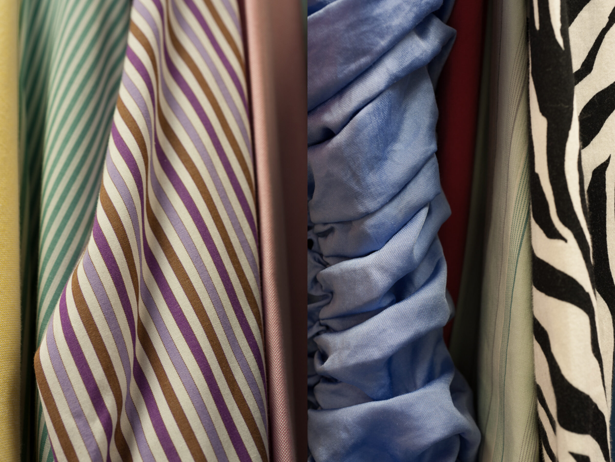 Close-up view of draped fabric samples displaying varied patterns: striped designs in purple, brown, and cream tones; solid-colored textiles in blue and burgundy; and bold zebra-stripe patterns in black and cream. The fabrics are arranged vertically with natural folds and shadows emphasizing their texture and dimensional quality.