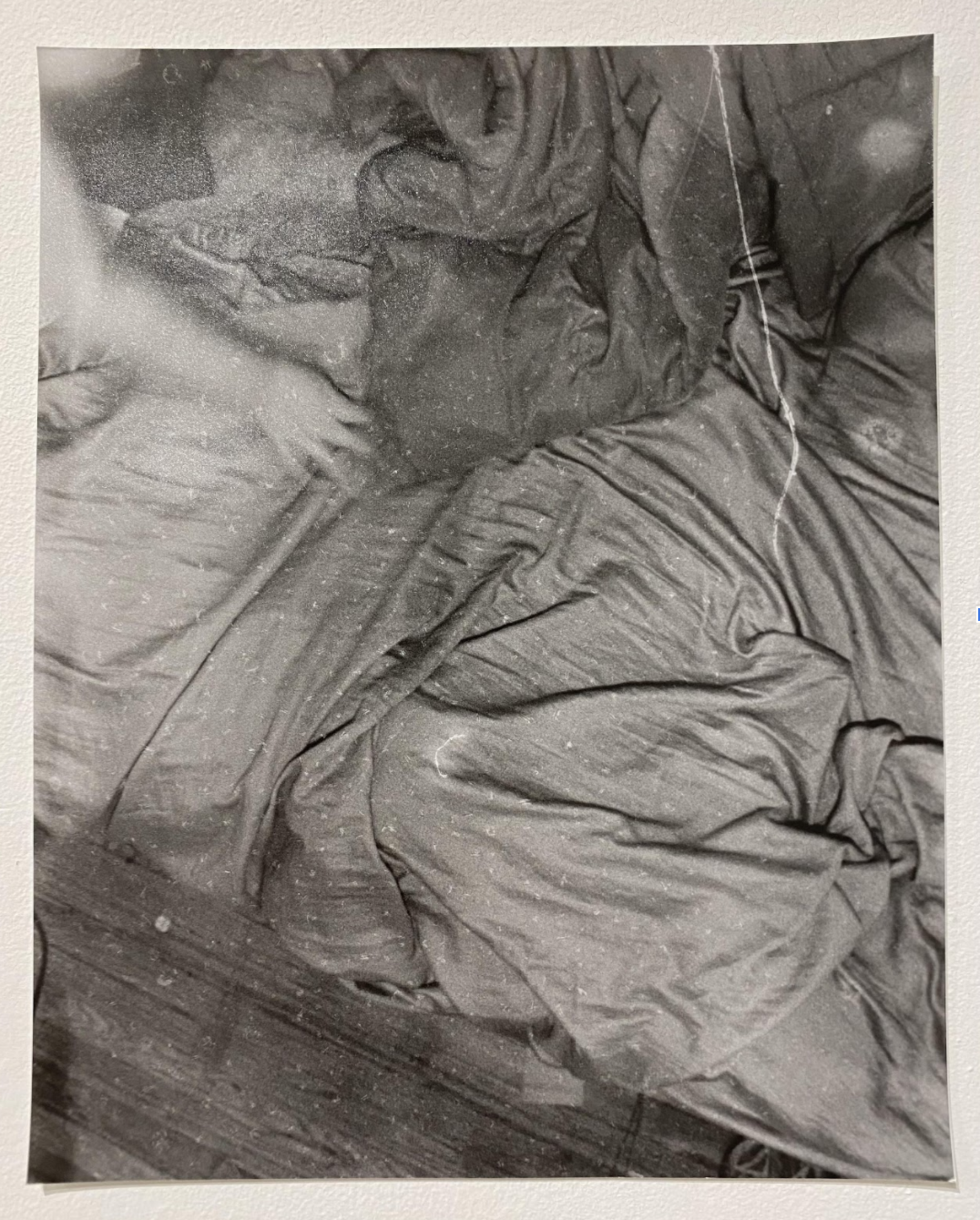 Black and white photograph of crumpled bedsheets and fabric, captured from above. The composition emphasizes the play of light and shadow across deep folds and wrinkles, creating an abstract study of texture and form in the tangled cloth.