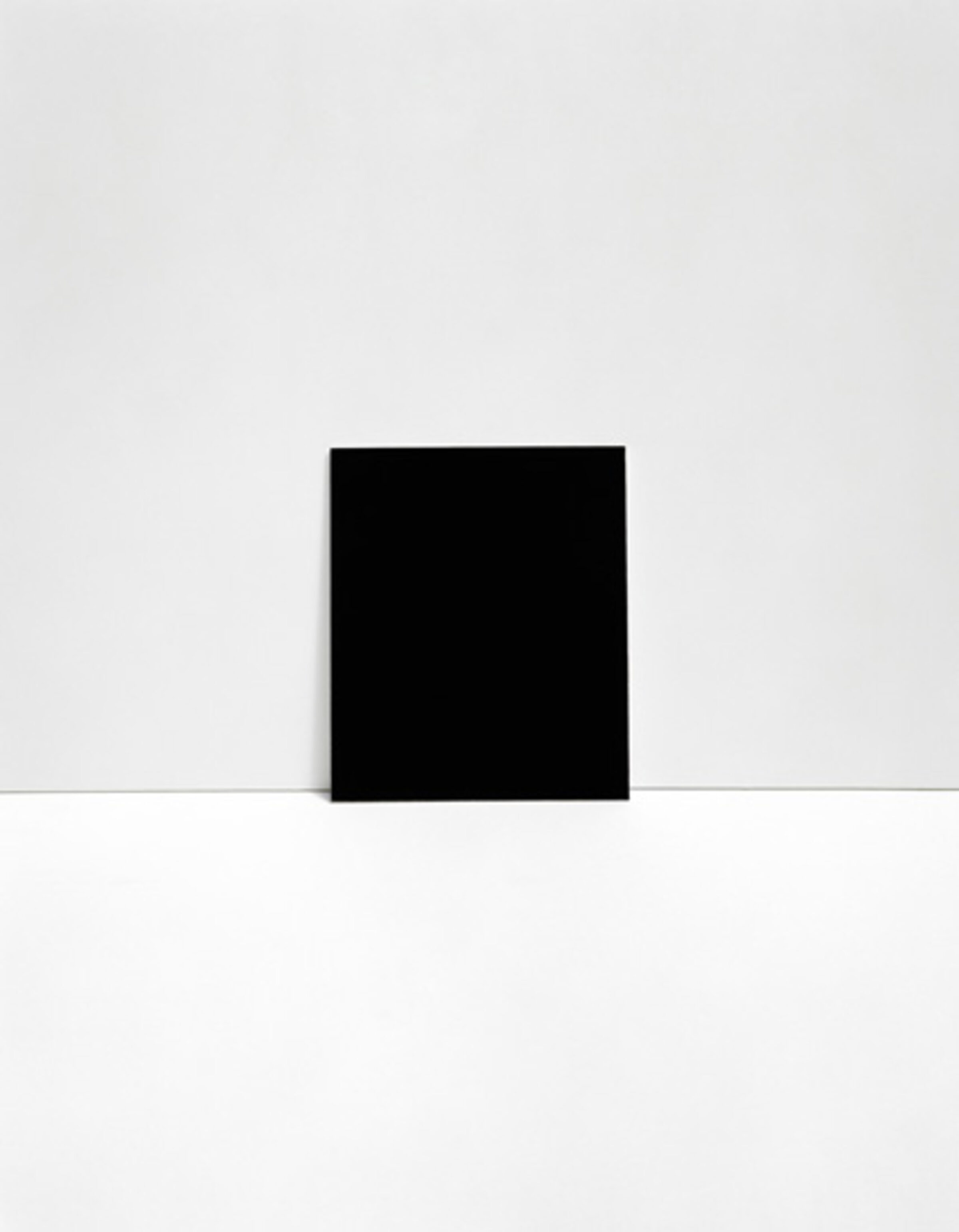 A black rectangular form positioned centrally against a light gray background, bisected horizontally by a darker gray line that suggests spatial division or a horizon line. The composition emphasizes minimalist geometry and tonal relationships.