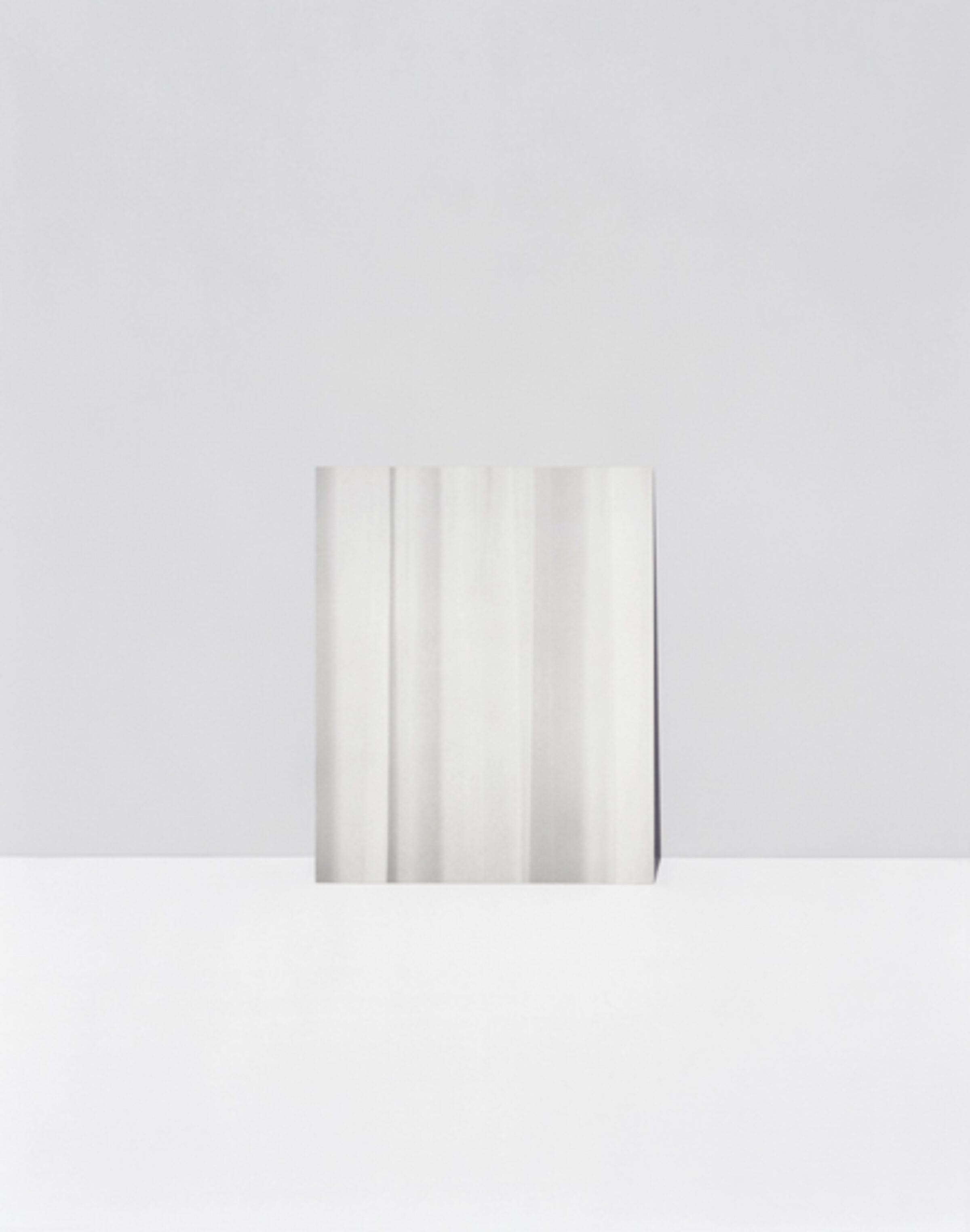 A minimalist composition featuring vertical folds or pleats of white and light gray material against a neutral gray background, creating subtle gradations of tone and shadow through gentle gradients and soft light.