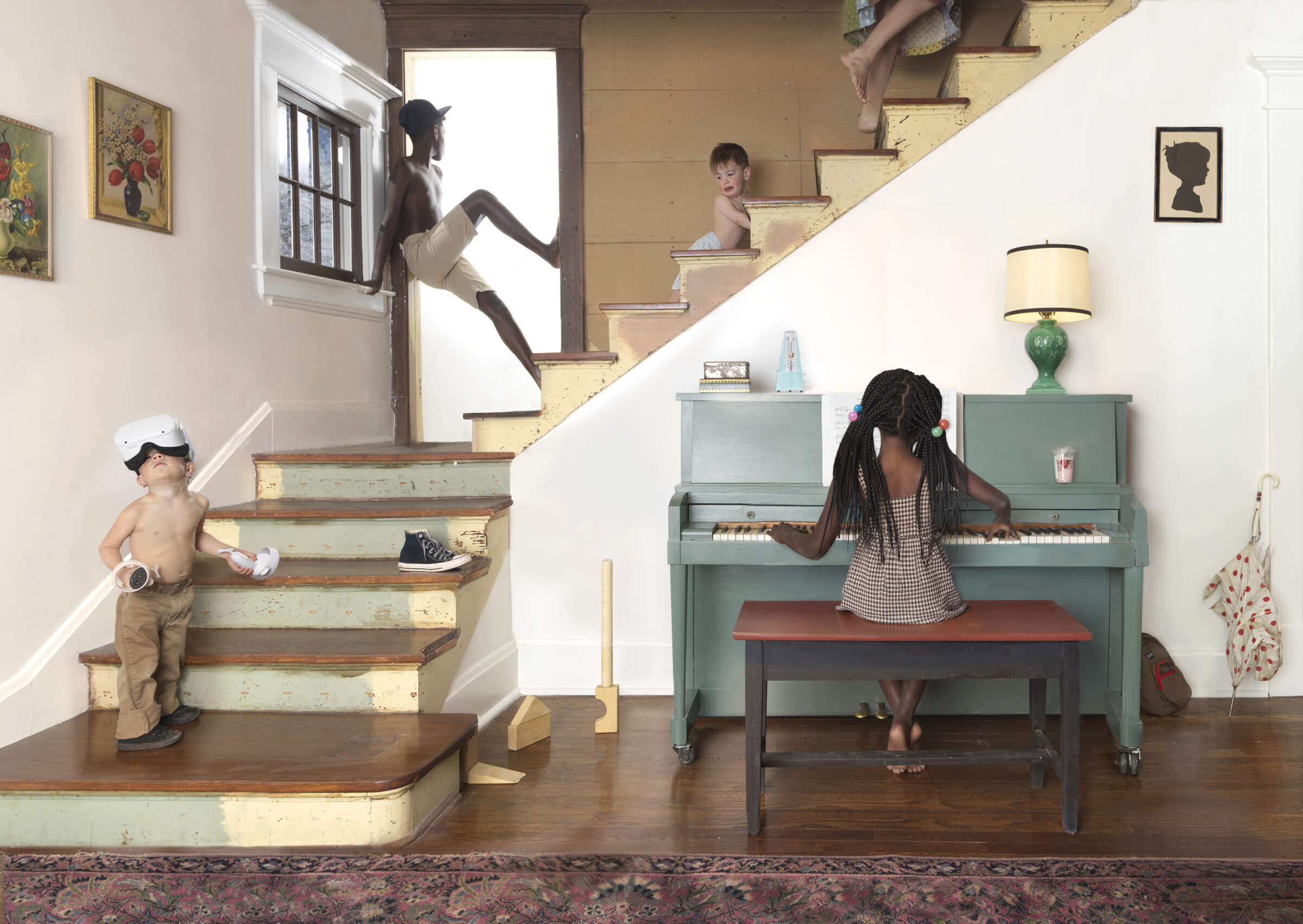 A staged domestic interior scene depicting multiple children engaged in various activities across different levels of a staircase and room. A child in a VR headset stands on the lower left stairs, another sits at a green piano in the center, while additional figures appear on the upper staircase and doorway. The composition combines realistic domestic furnishings—including framed artwork, a lamp, and patterned rug—with surreal spatial arrangements and the children's varied states of dress and pose.