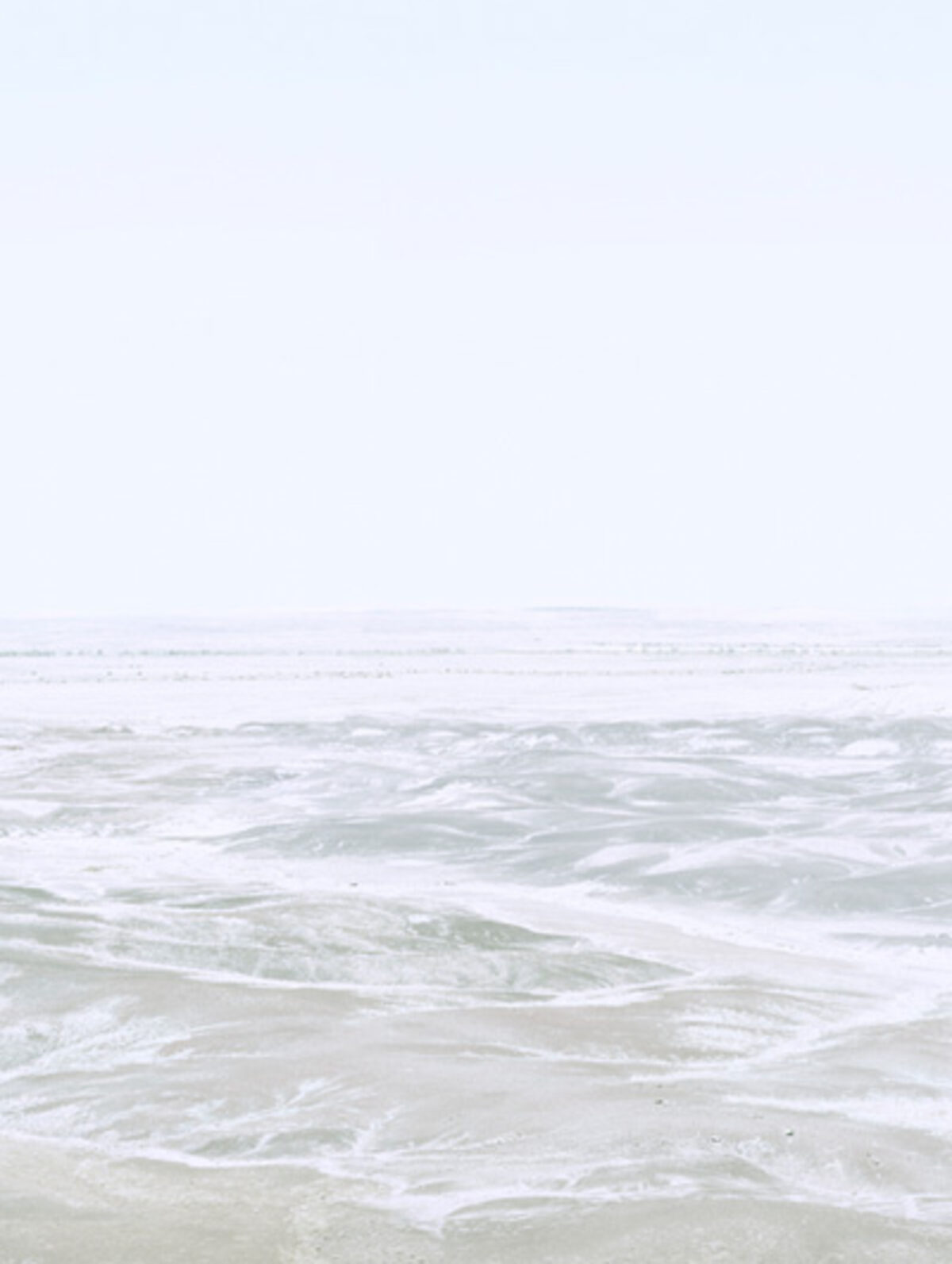 Soft, hazy seascape with gentle waves and foam washing onto a pale sandy beach beneath an overcast sky, rendered in muted tones of white, gray, and soft green in a minimalist composition.