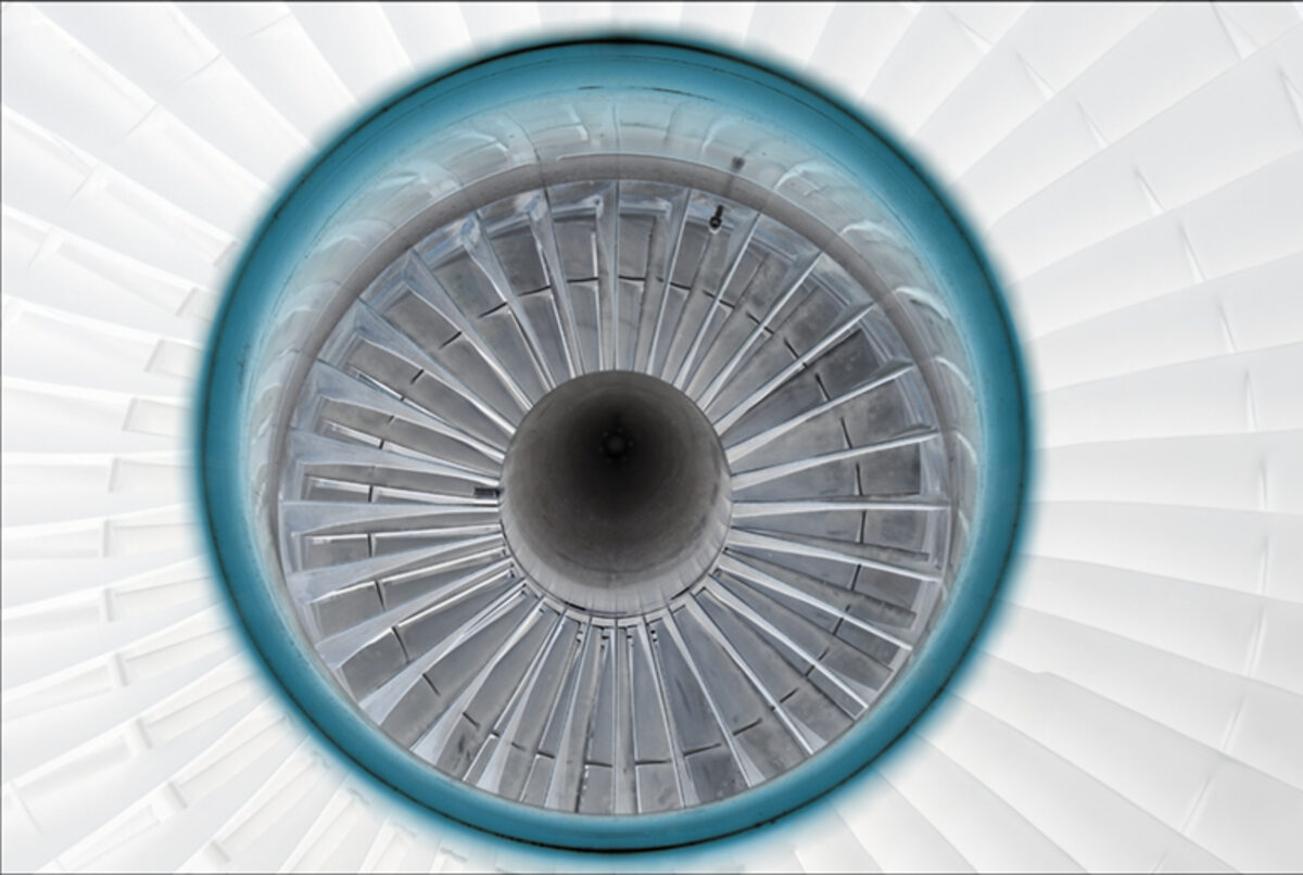 Symmetrical overhead view of a jet engine intake, featuring concentric rings of metal blades radiating from a dark central core, framed by a turquoise outer ring against a pale geometric background.