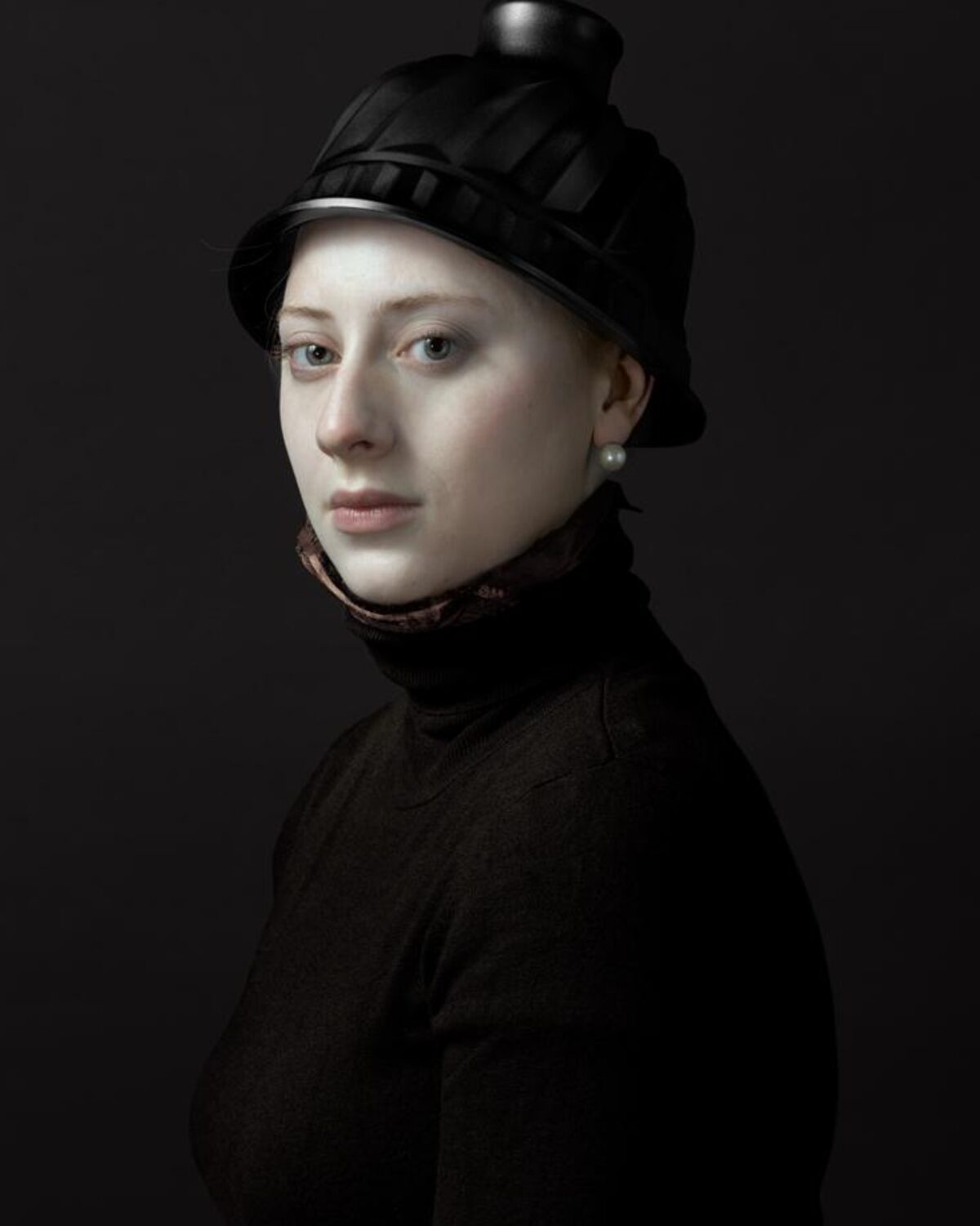 Portrait of a young woman wearing a black turtleneck and ornate black hat with decorative band, set against a dark background. She gazes toward the camera with a composed expression, her pale complexion and pearl earring subtly illuminated by controlled lighting that emphasizes the painting's classical Renaissance-inspired style.