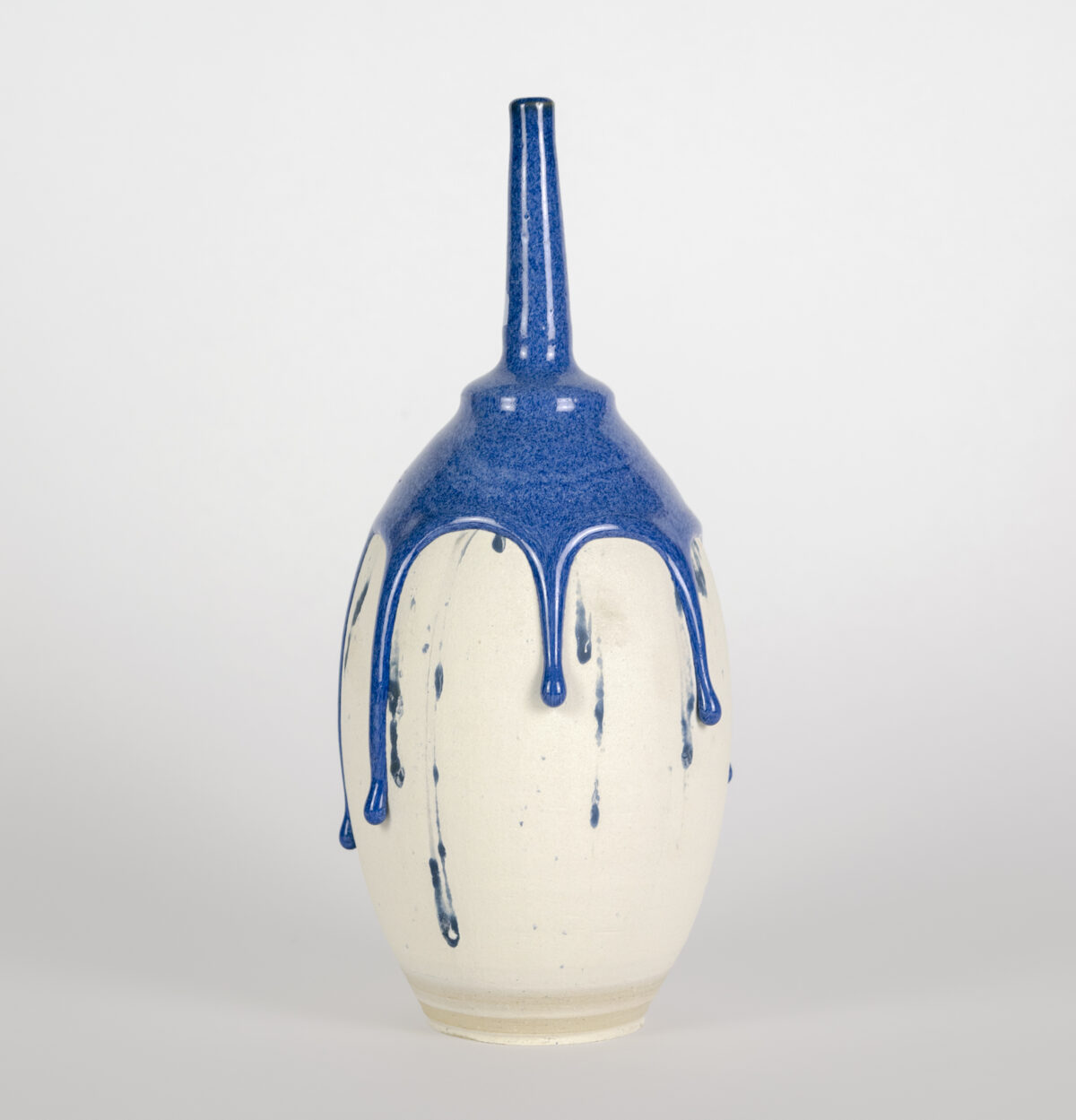 A cream-colored ceramic vessel with a rounded body and tapered neck, finished with a glossy blue glaze on the upper portion that drips downward in organic streaks against the pale surface below.