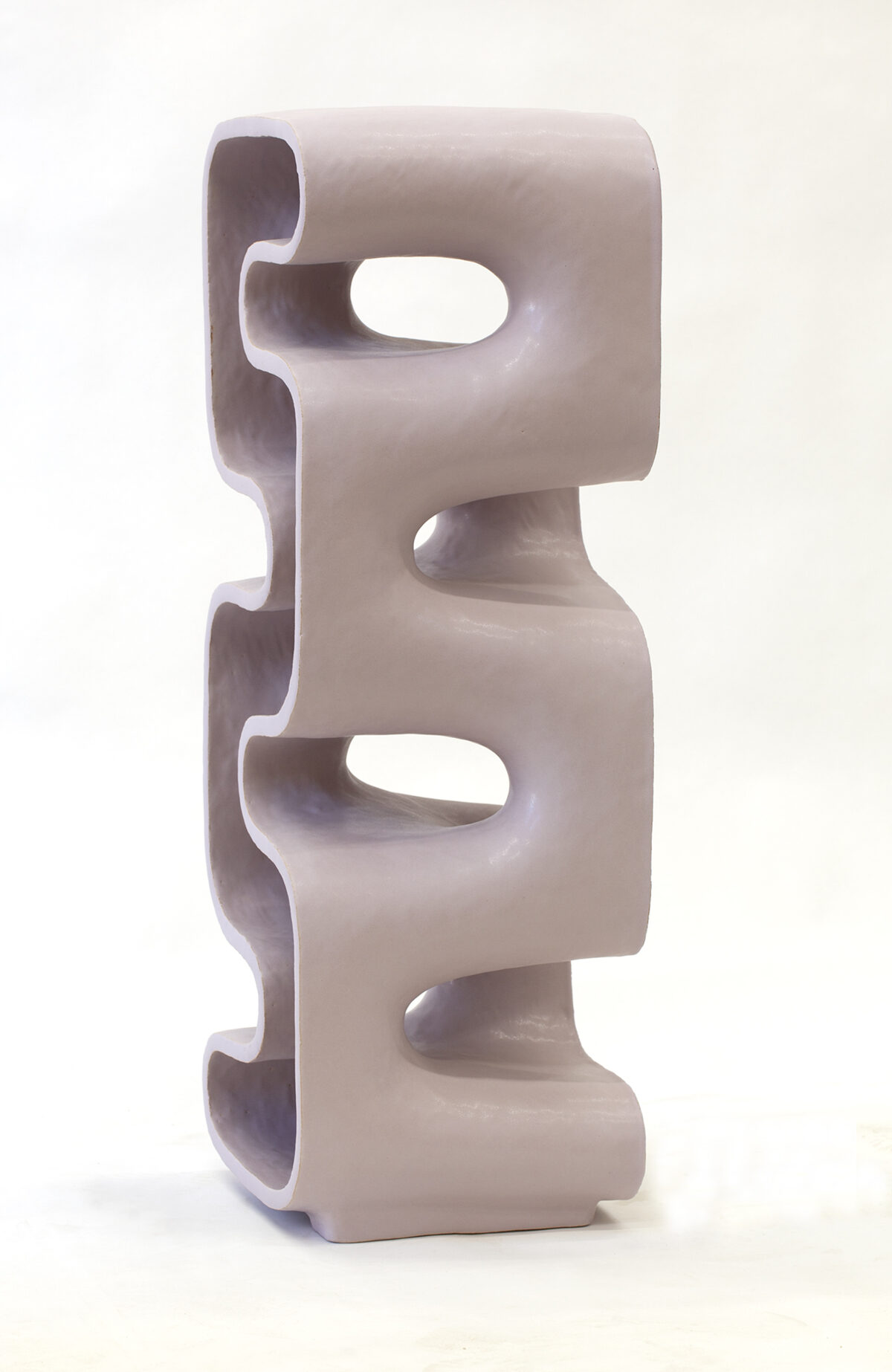 Stacked ceramic form with a pale mauve finish, featuring two squared-off sections connected by curved cylindrical elements. Each section is punctuated by oval cutouts that create negative spaces, revealing the hollow interior and casting subtle shadows across the glazed surface.