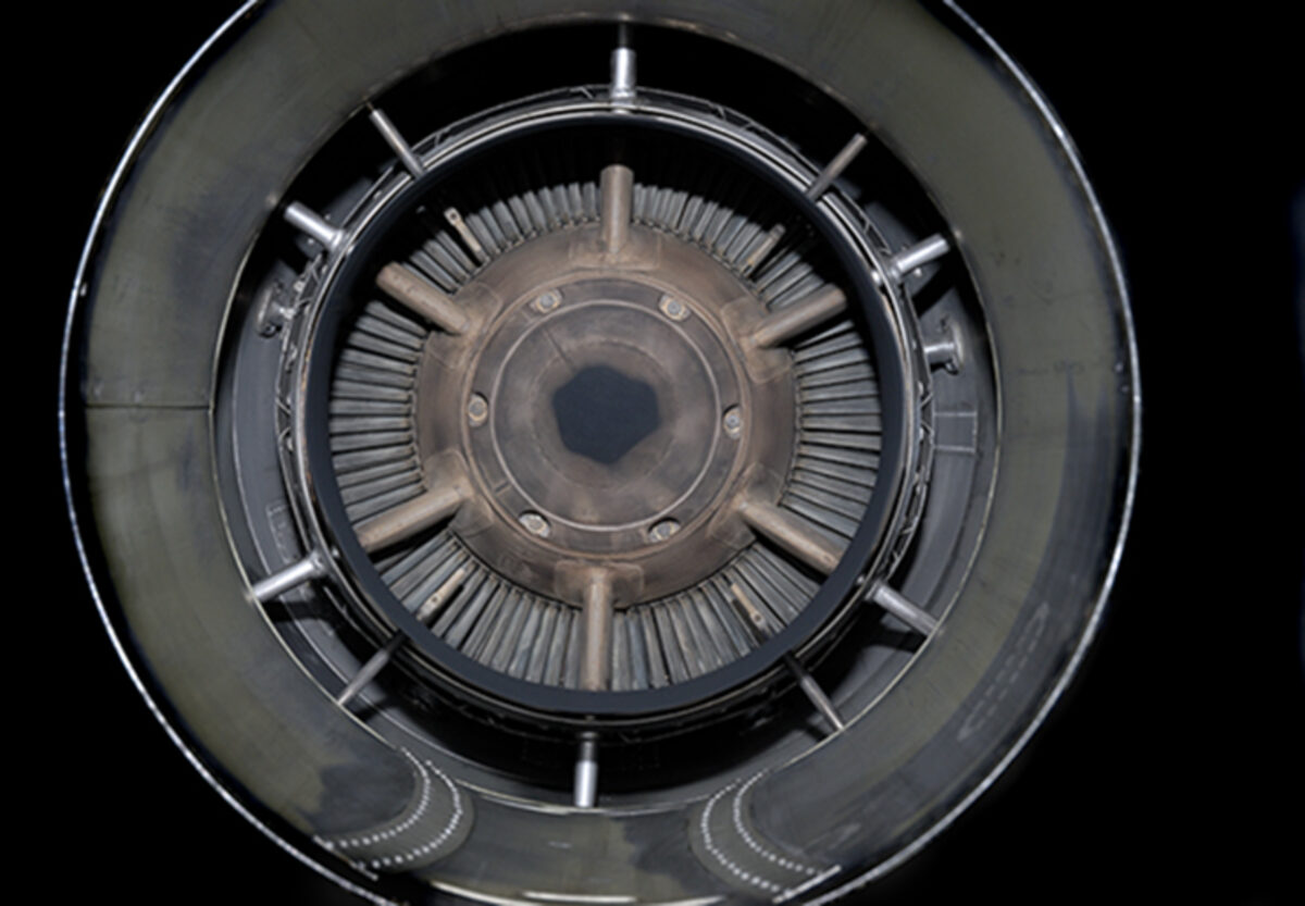 Concentric circular view of a mechanical turbine or engine intake, rendered in grayscale. Radiating fins and metallic components create a hypnotic, symmetrical pattern receding toward a dark central aperture, photographed directly from above against a black background.