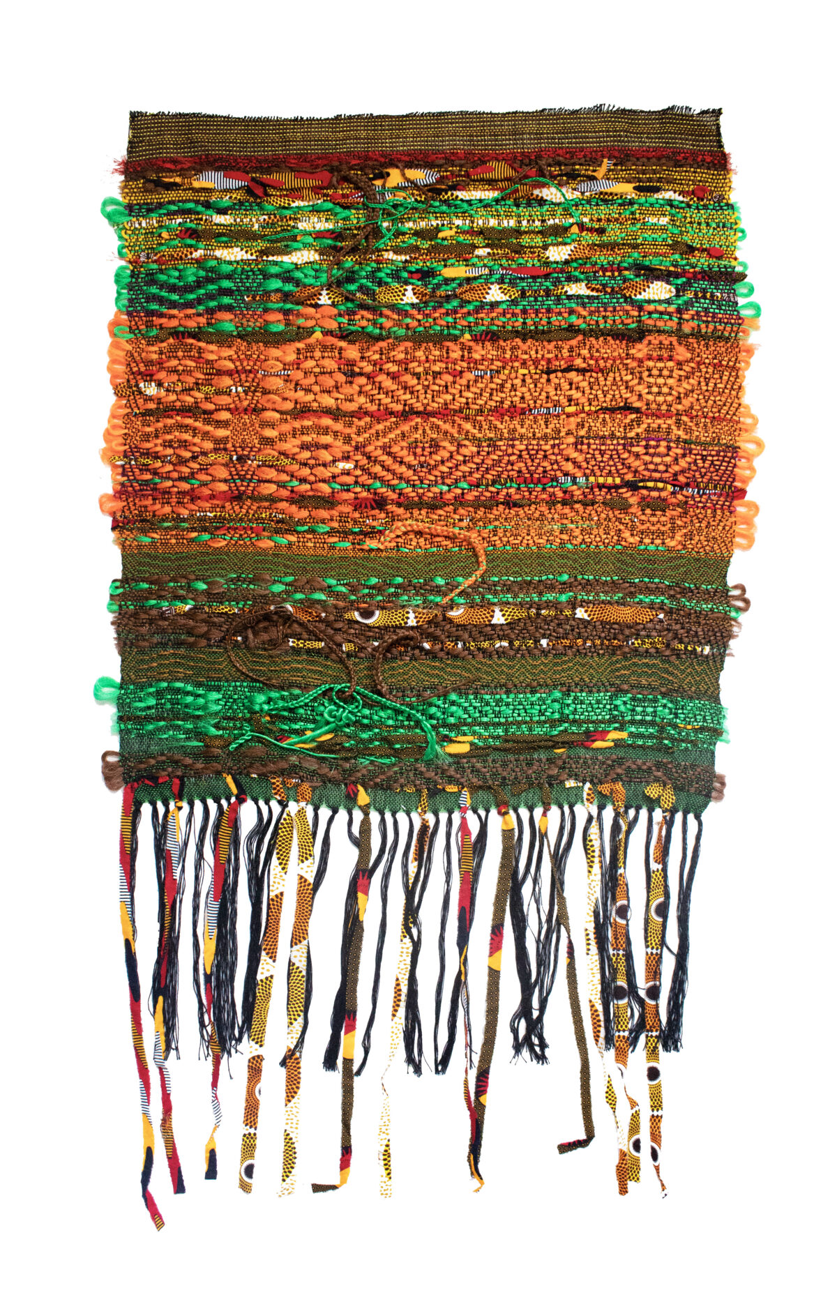 Layered horizontal bands of woven and textile materials in earthy tones of brown, orange, green, and gold, with decorative green pom-poms along the edges and multicolored braided fringe hanging from the bottom.