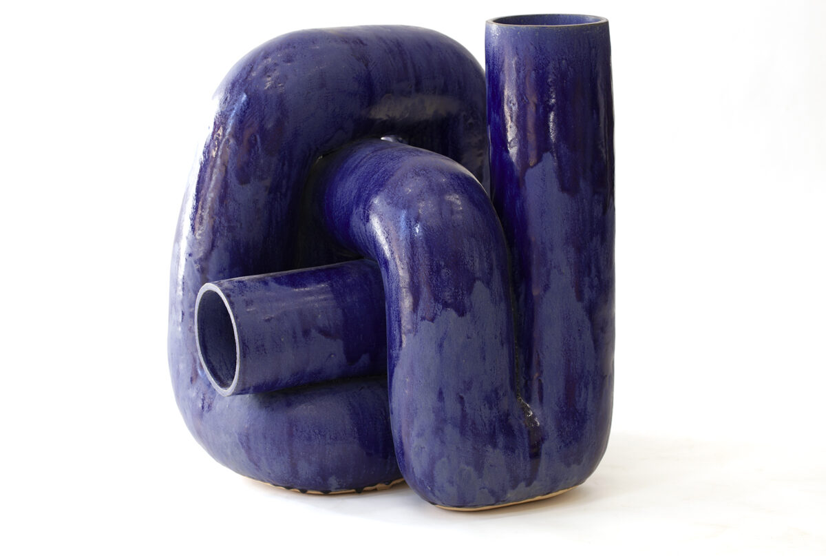 Three abstract ceramic vessels in deep blue glaze arranged in an organic cluster. The forms feature curved, interlocking shapes with smooth, flowing surfaces and glossy finishes, creating a sculptural composition with negative spaces and openings between the elements.