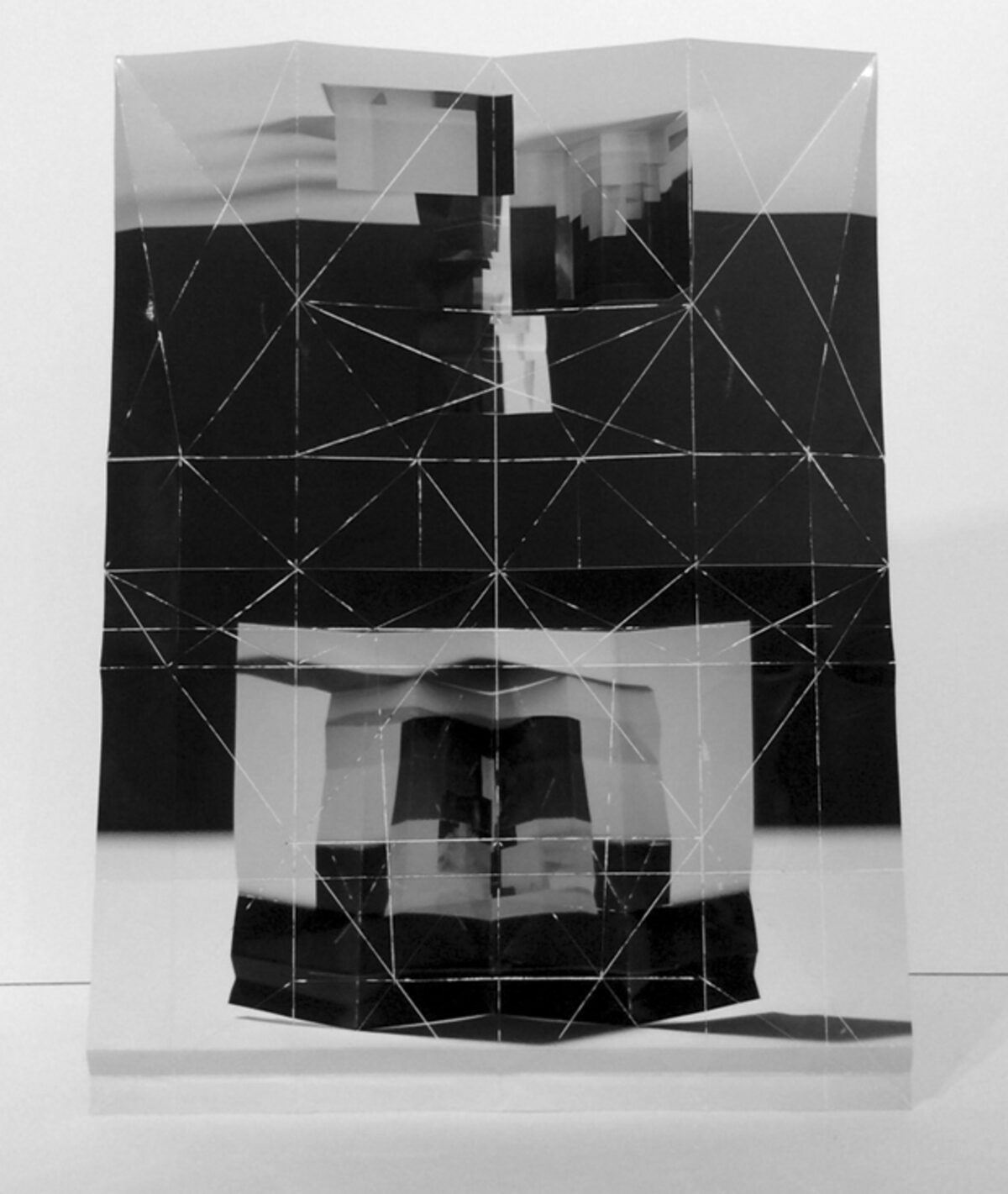 Black and white folded and layered printed paper construction featuring geometric line drawings overlaid on architectural imagery, creating a three-dimensional collage with alternating planes of transparent and opaque sections that reveal fragmented views of urban buildings.