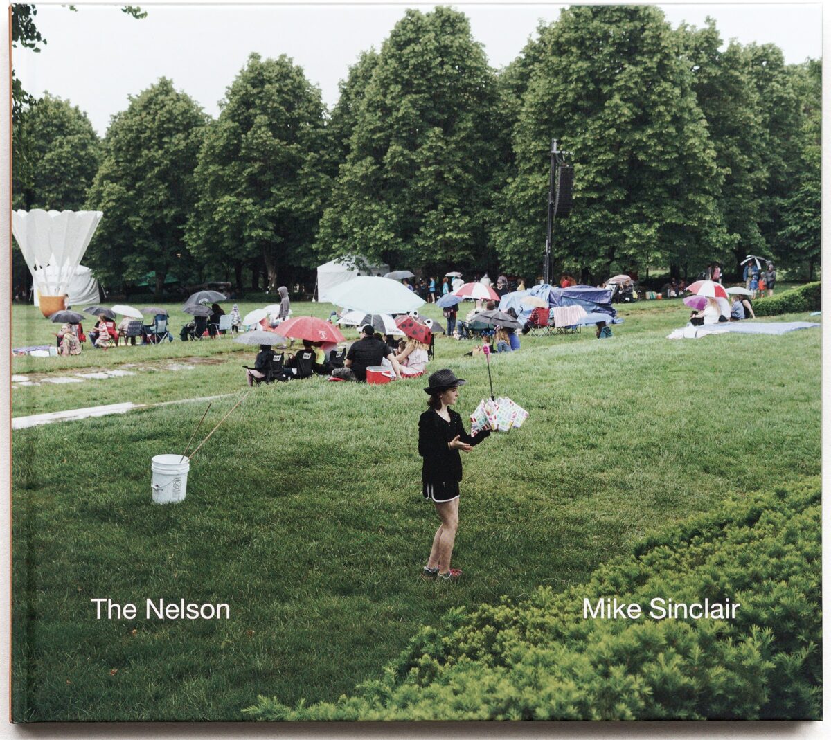 Front cover of The Nelson by Mike Sinclair, a photograph of visitors with umbrellas on the lawn of the Nelson-Atkins Museum of Art.
