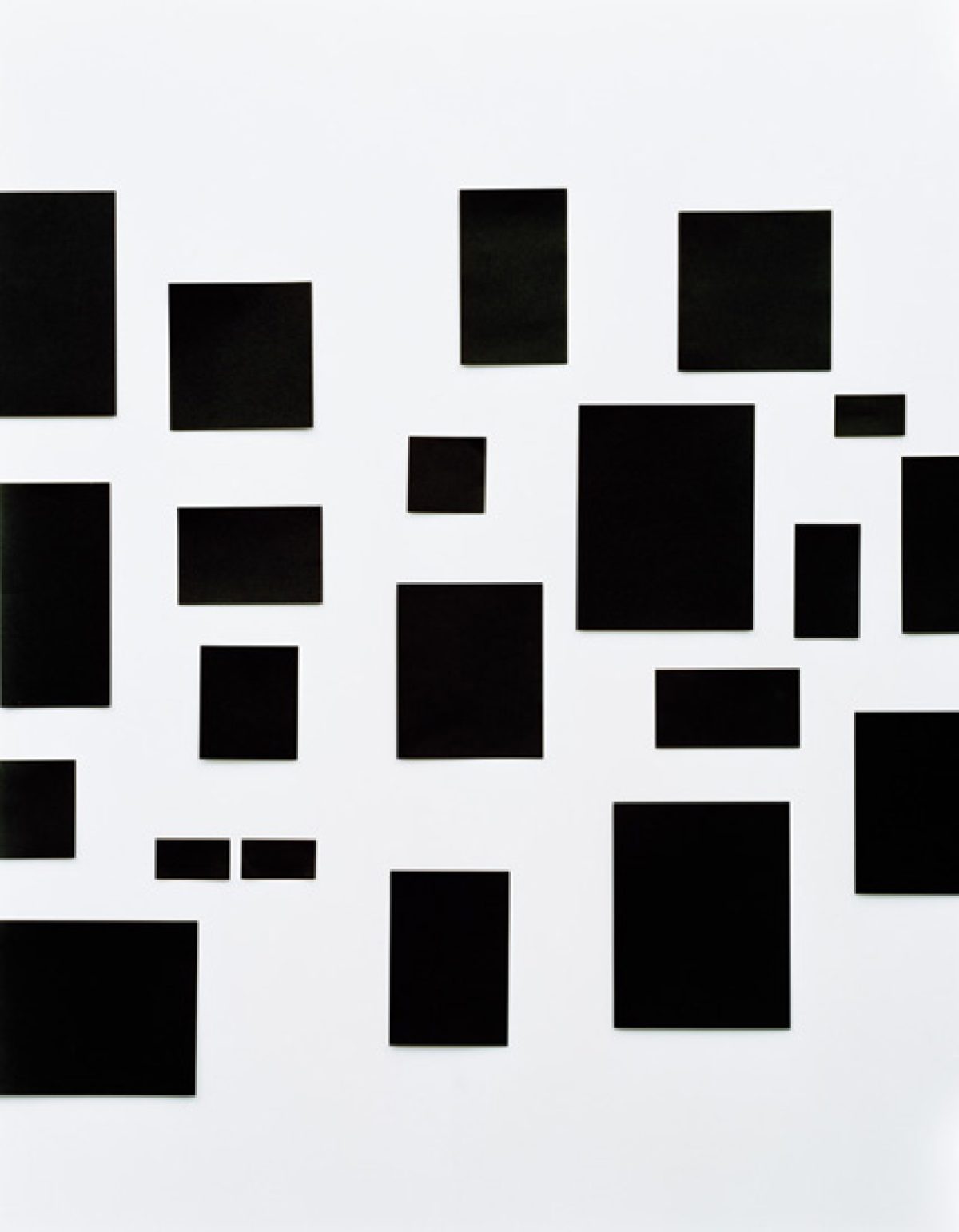 Abstract composition of scattered black rectangular forms of varying sizes arranged across a light gray background, creating a fragmented, geometric spatial arrangement.