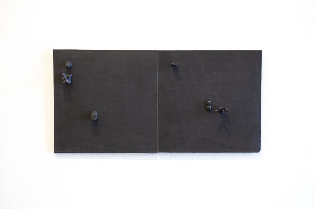 Two dark matte ceramic panels mounted side by side on a white wall, each fitted with metallic knobs and hardware. The left panel features two circular knobs positioned vertically, while the right panel has a similar knob with an additional key or lever mechanism, creating an austere, minimalist composition suggestive of functional cabinetry.