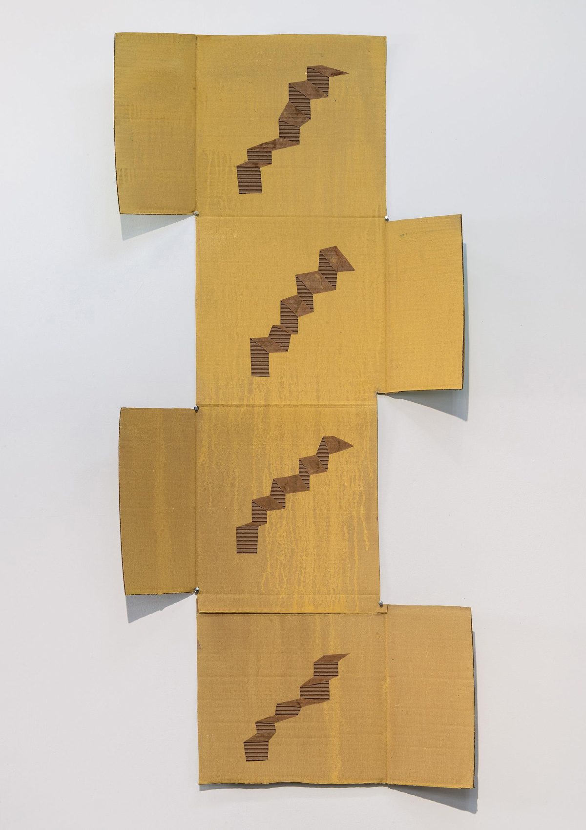 Four tan cardboard panels arranged vertically and offset from each other against a white wall, each featuring a staircase pattern cut through the corrugated material to reveal the layered interior. The cascading geometric forms progress upward across the composition, creating a sense of movement through the dimensional cutouts.