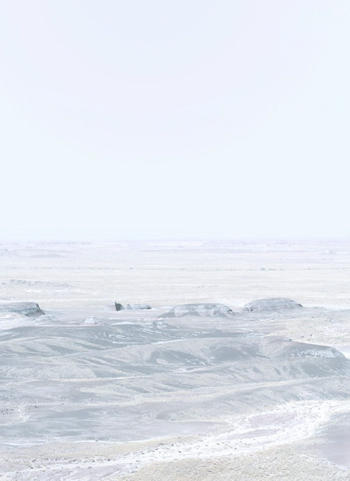 Minimalist coastal landscape with layered horizons of pale gray and white tones. Rocky outcroppings and sandy beach dissolve into misty atmosphere, creating a subtle, almost monochromatic composition that emphasizes atmospheric depth and geometric abstraction.