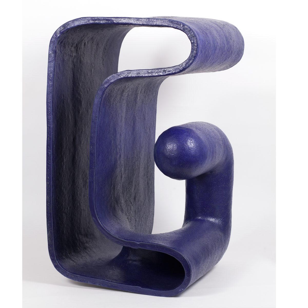 A deep blue ceramic sculpture with a glossy glaze featuring an abstract, organic form that resembles a stylized finger or curved gesture. The piece has smooth, rounded surfaces with hollow sections and a bulbous protrusion, creating a dynamic three-dimensional composition against a white background.
