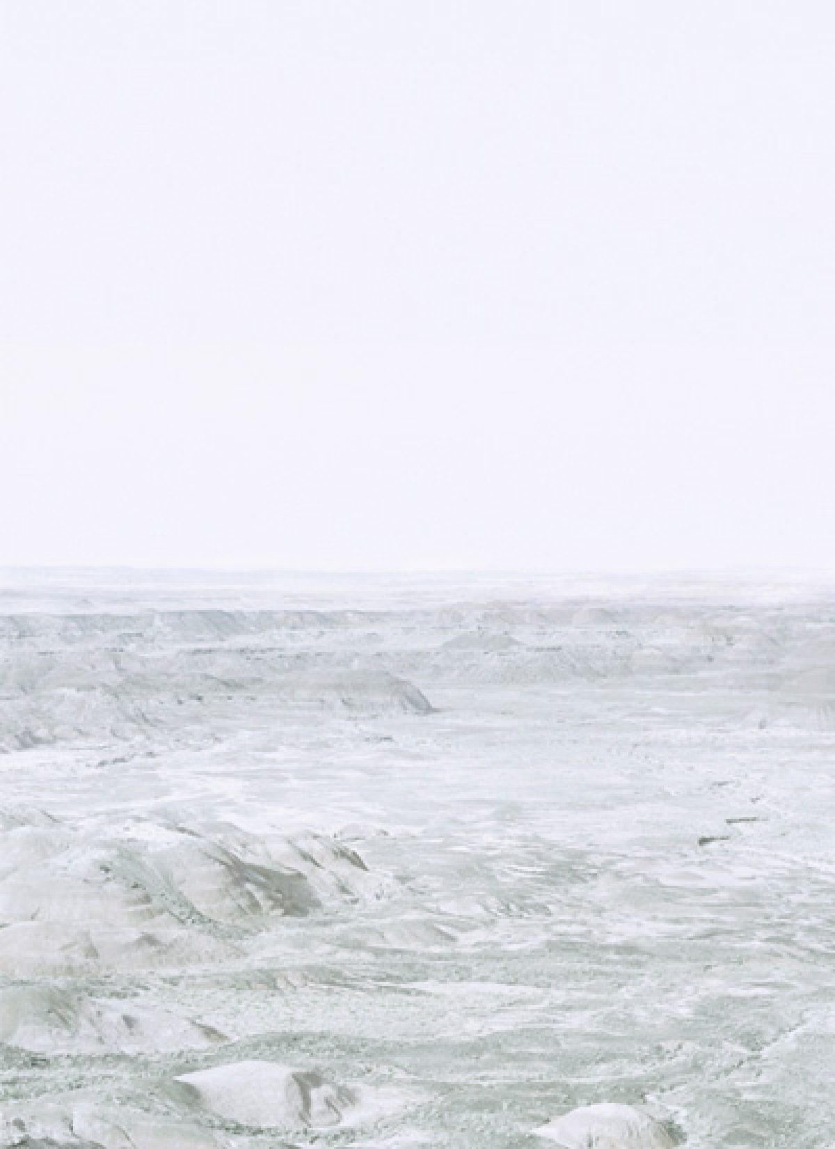 Ethereal landscape photograph of an expansive, barren terrain with undulating hills rendered in soft whites, grays, and pale greens beneath a hazy, overexposed sky. The composition creates an abstracted, almost monochromatic vista that blurs the distinction between earth and atmosphere.