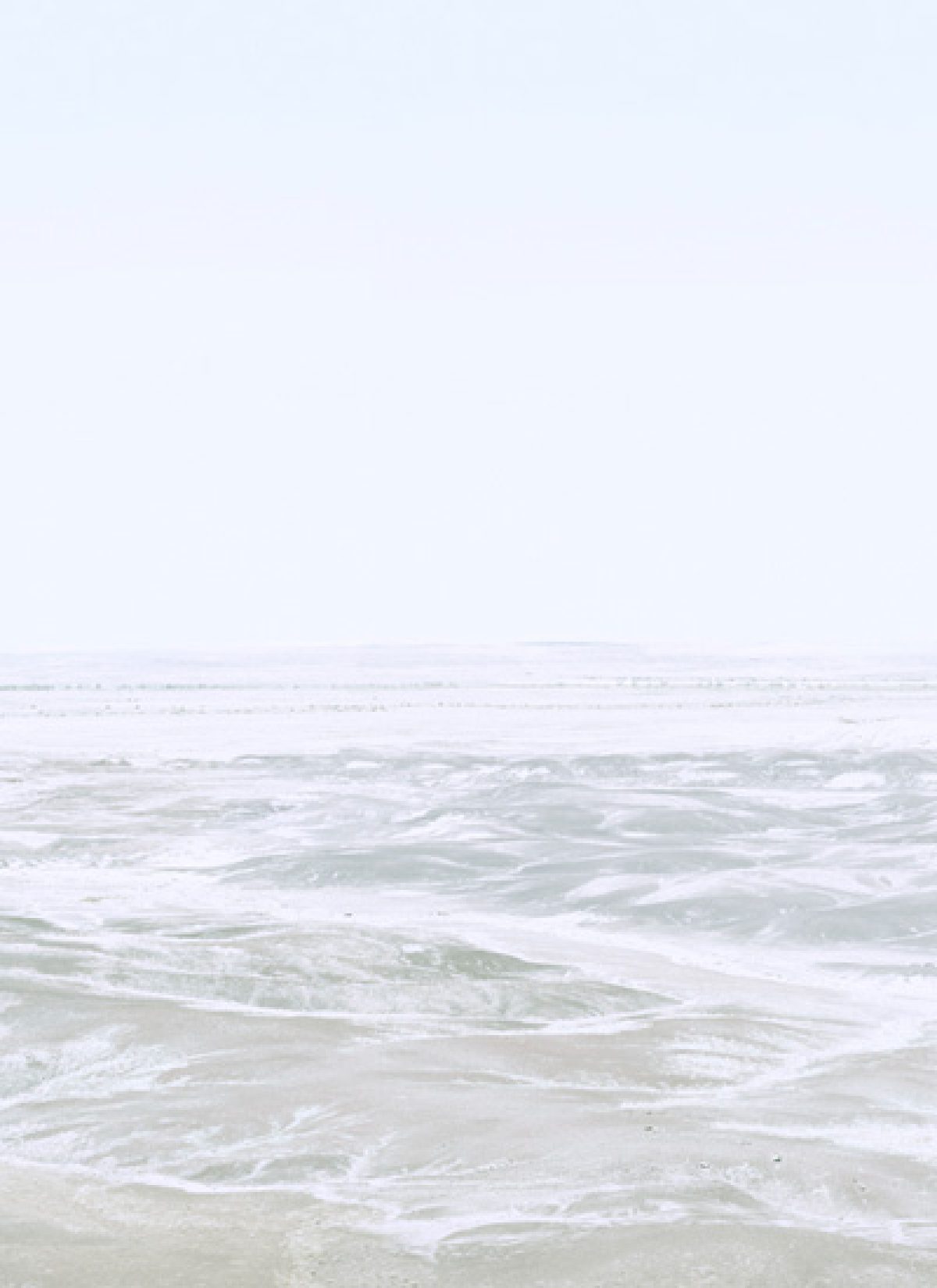 Soft, hazy seascape with gentle waves and foam washing onto a pale sandy beach beneath an overcast sky, rendered in muted tones of white, gray, and soft green in a minimalist composition.
