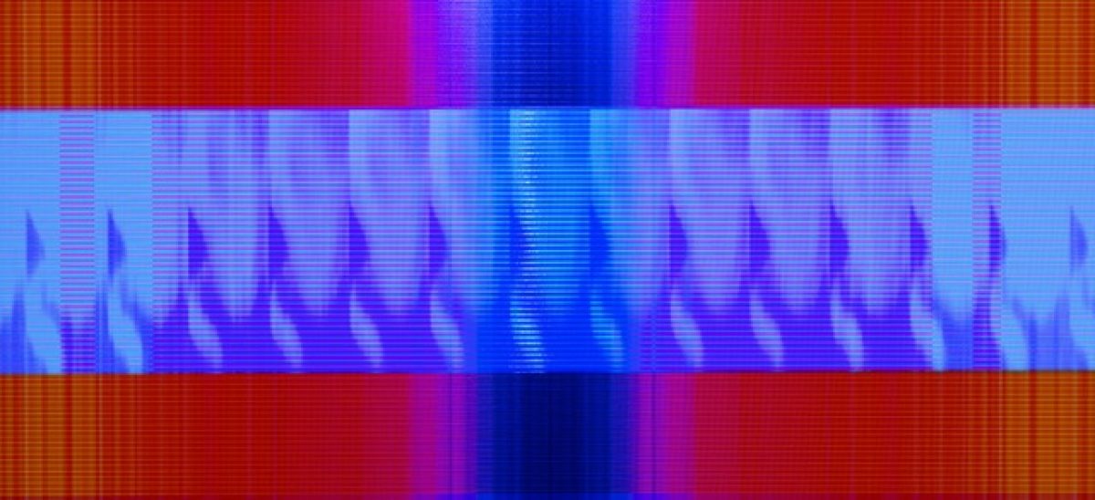 Horizontal composition with vibrant gradient bands of red, orange, pink, magenta, and blue, featuring a central section of lighter blue with repeating vertical flame-like or wave patterns in darker blue. Fine horizontal scan lines run throughout, creating a digital or electronic visual quality.