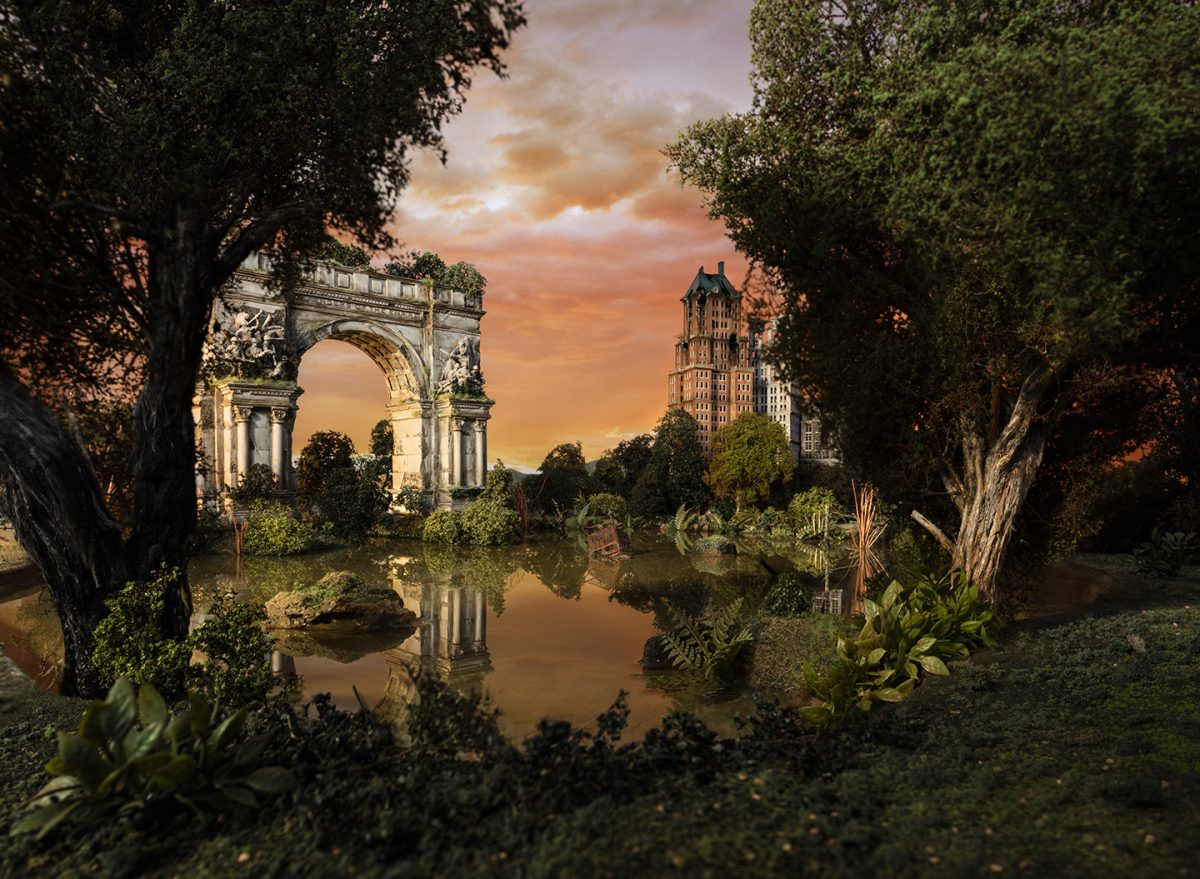 A meticulously composed landscape featuring an ornate classical archway framed by towering trees on either side of a reflective water channel. In the distance, a tall Art Deco building rises against an amber and orange sunset sky, creating a dreamlike tableau that blends architectural grandeur with lush vegetation and atmospheric light.