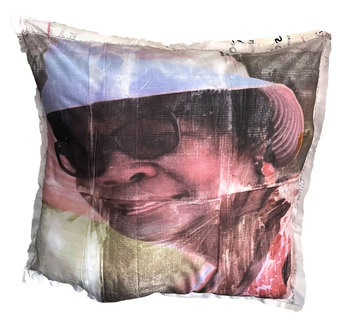 A translucent textile pillow features a portrait of a woman wearing sunglasses, rendered in soft pink, blue, and dark tones. The image appears layered and ethereal, with the figure's face and upper body visible through the semi-transparent fabric material, creating an atmospheric, dreamlike quality.