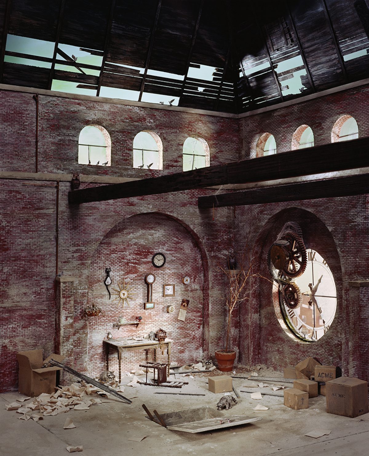 An abandoned brick interior with a partially collapsed ceiling reveals sky through broken wooden beams. A large gear-driven clock face protrudes from the right wall, while the left alcove displays hanging clocks and mechanical objects amid scattered debris and cardboard boxes labeled "ACME" on the floor below.