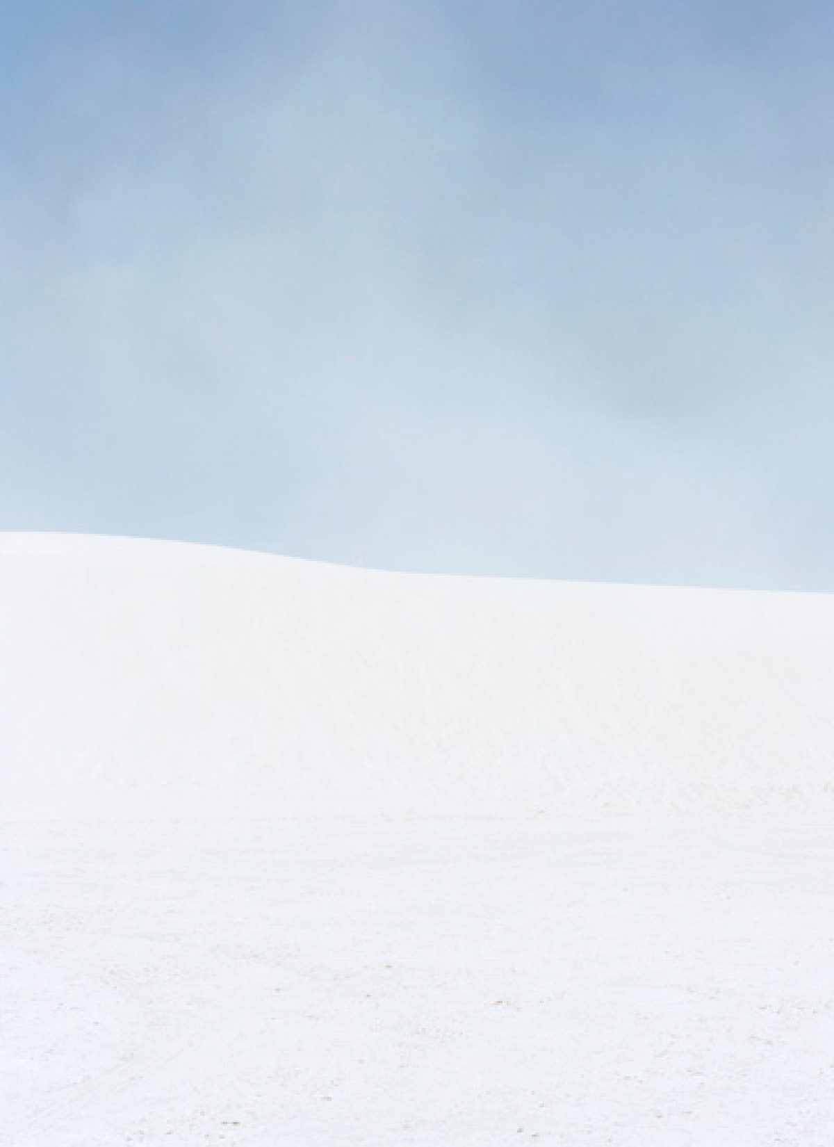 A minimalist landscape divided horizontally into two zones: a soft blue-gray sky occupying the upper portion, and a vast expanse of white snow or sand below, with subtle variations in tone creating gentle undulations across the lower plane.