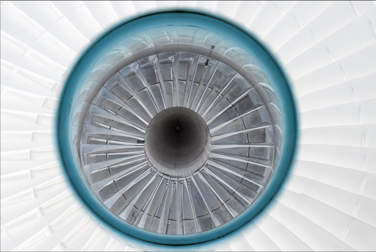 Symmetrical overhead view of a jet engine intake, featuring concentric rings of metal blades radiating from a dark central core, framed by a turquoise outer ring against a pale geometric background.
