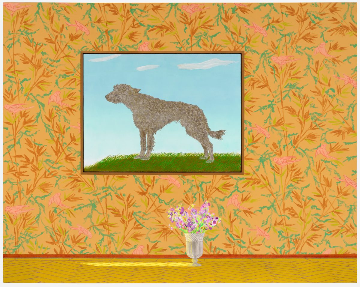 A framed portrait of a gray, shaggy dog standing on green grass against a blue sky hangs on a vibrant wallpapered wall with orange and pink botanical patterns. Below the framed work sits a classical urn containing purple flowers on a yellow wooden floor.