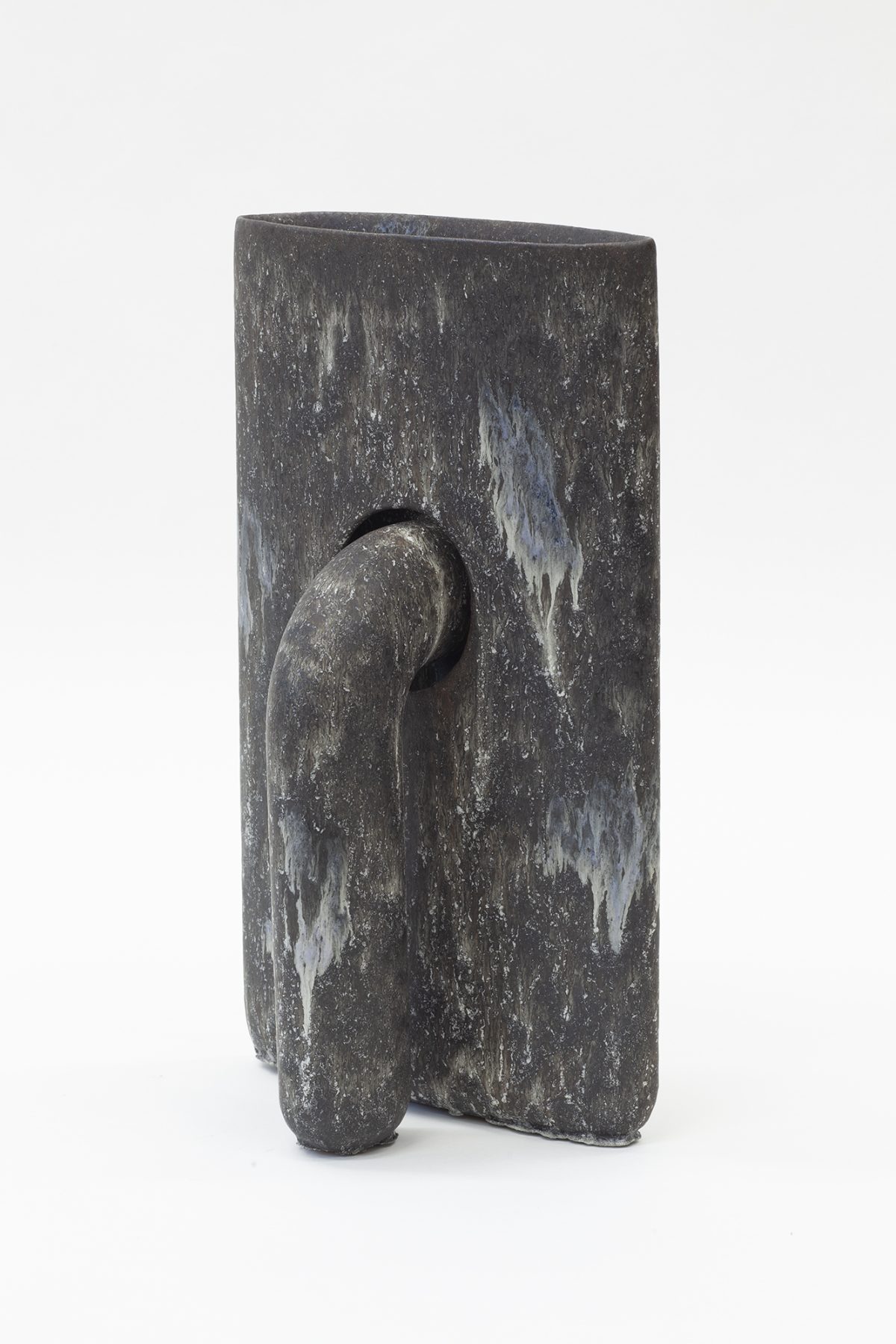 Dark gray stoneware vessel with a rectangular body featuring weathered white streaking across its surface. A curved, organic form protrudes from the front, creating an abstract sculptural composition that suggests both natural and figural elements.