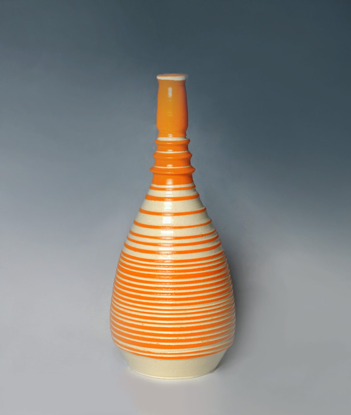 A tall ceramic vessel with a teardrop-shaped body featuring horizontal orange and cream stripes, topped with a narrow cylindrical neck in solid orange glaze against a neutral gray background.