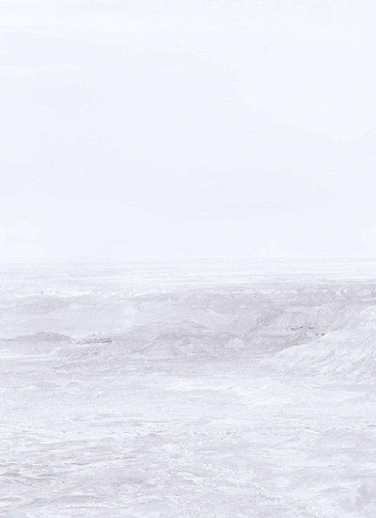 Minimalist landscape featuring layered, undulating terrain in soft whites and grays beneath a pale, overcast sky. The composition emphasizes subtle tonal variations and atmospheric haze across an expansive, largely featureless vista.