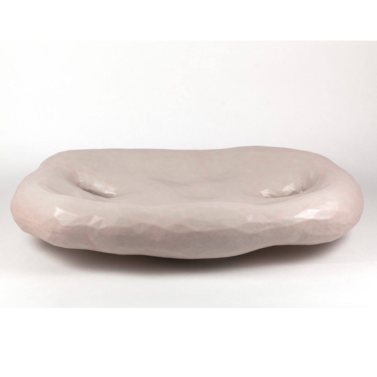 A pale pink ceramic bowl with an organic, elongated form featuring two shallow indentations across its curved surface, finished with a subtle gloss glaze.