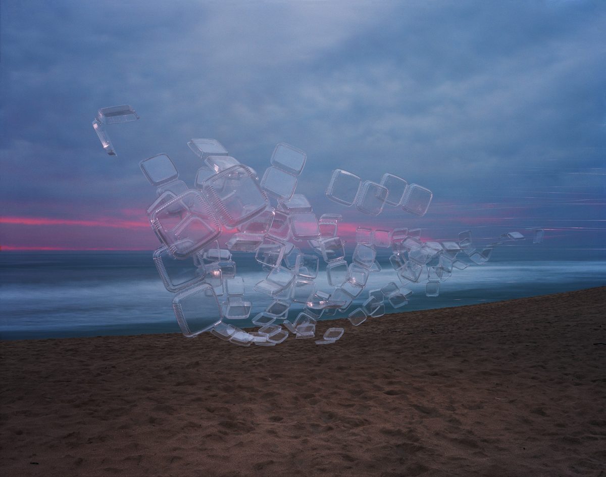 Translucent plastic takeout containers arranged in a sculptural pile on a beach at dusk, glowing with pink and blue light against a twilight sky and calm ocean horizon.