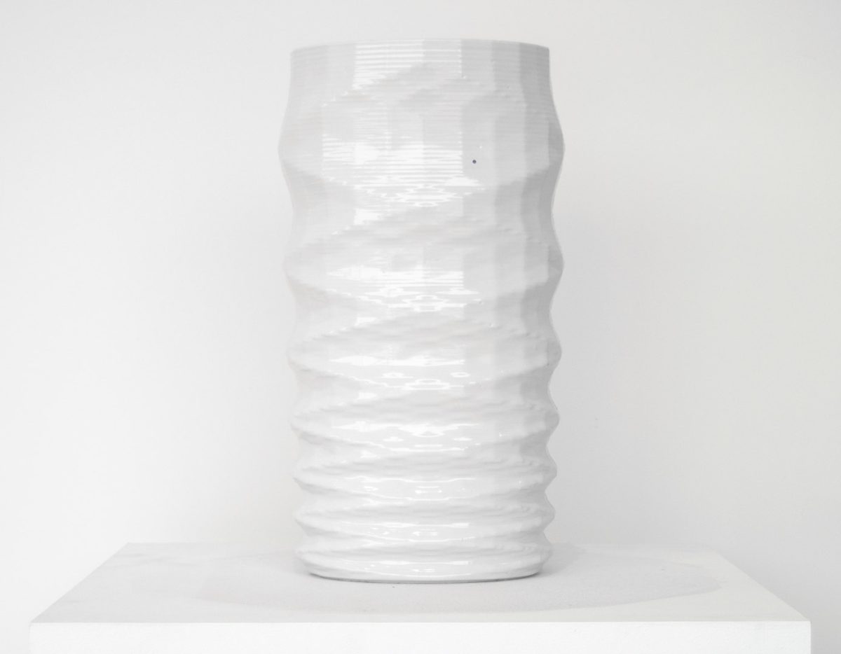A tall cylindrical porcelain vessel with a twisted, ribbed surface creating a helical pattern. The piece is rendered entirely in white glaze with subtle shadows emphasizing its spiraling form, displayed against a neutral background on a white platform.