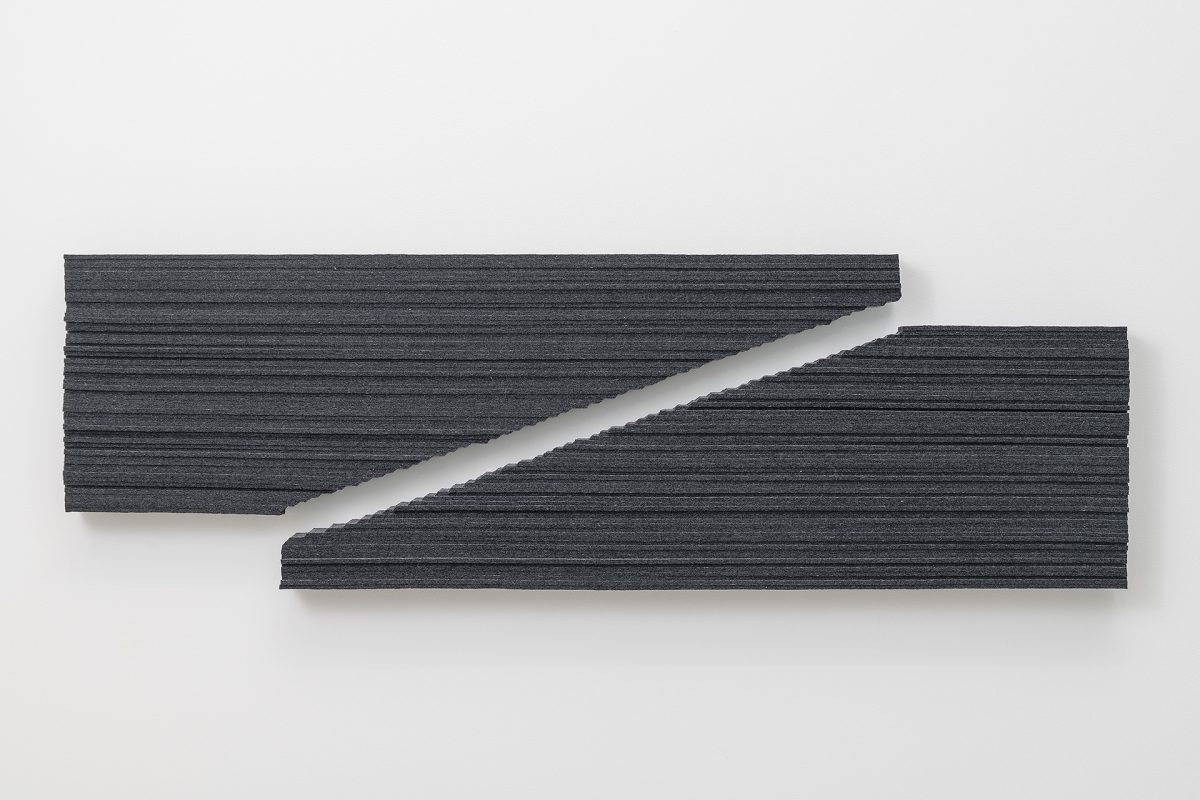 Two dark gray textile strips with horizontal ribbed texture are mounted on a white wall, angled diagonally across one another to create an interlocking geometric composition with a white gap between them.