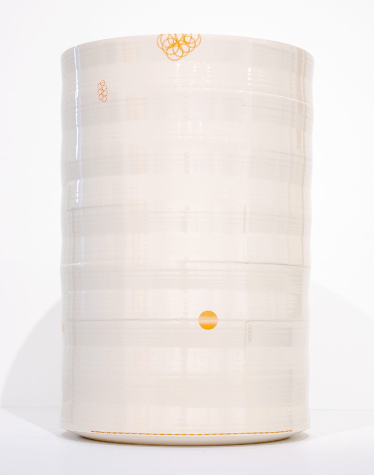 A cream-colored cylindrical porcelain vessel with horizontal ridges and delicate orange line drawings scattered across its surface, including abstract scribbled motifs near the top and a solid circle positioned on the lower section. The vase is photographed against a white background with subtle shadowing.