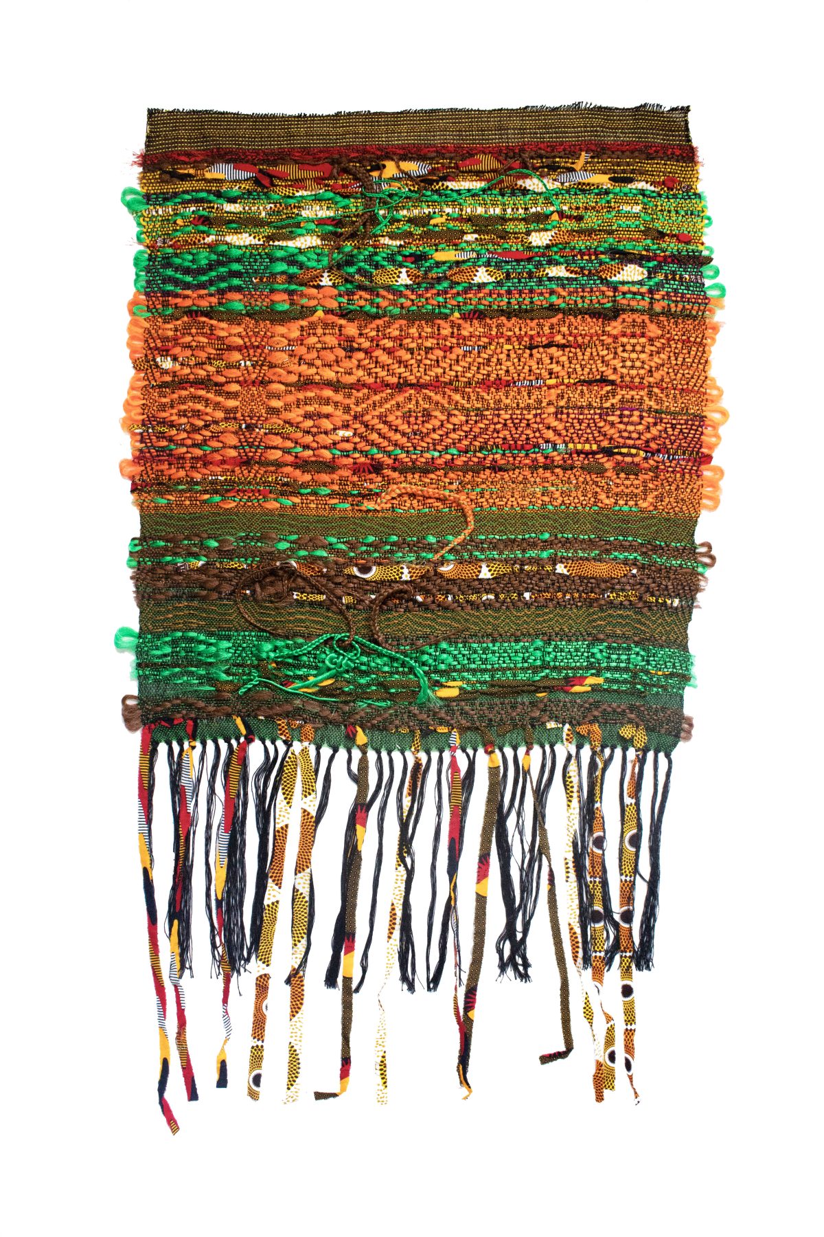 Layered horizontal bands of woven and textile materials in earthy tones of brown, orange, green, and gold, with decorative green pom-poms along the edges and multicolored braided fringe hanging from the bottom.